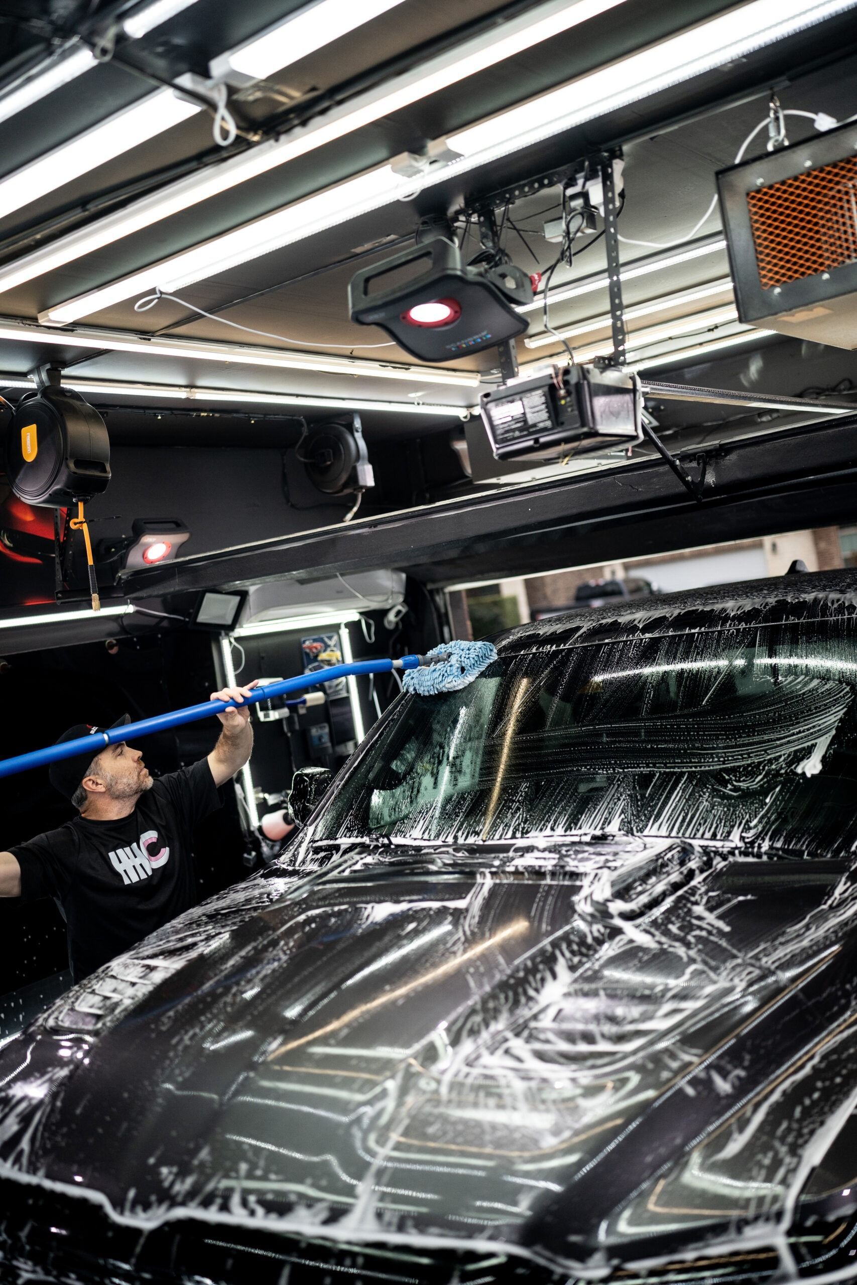 A man is washing a car with a hose in a garage.