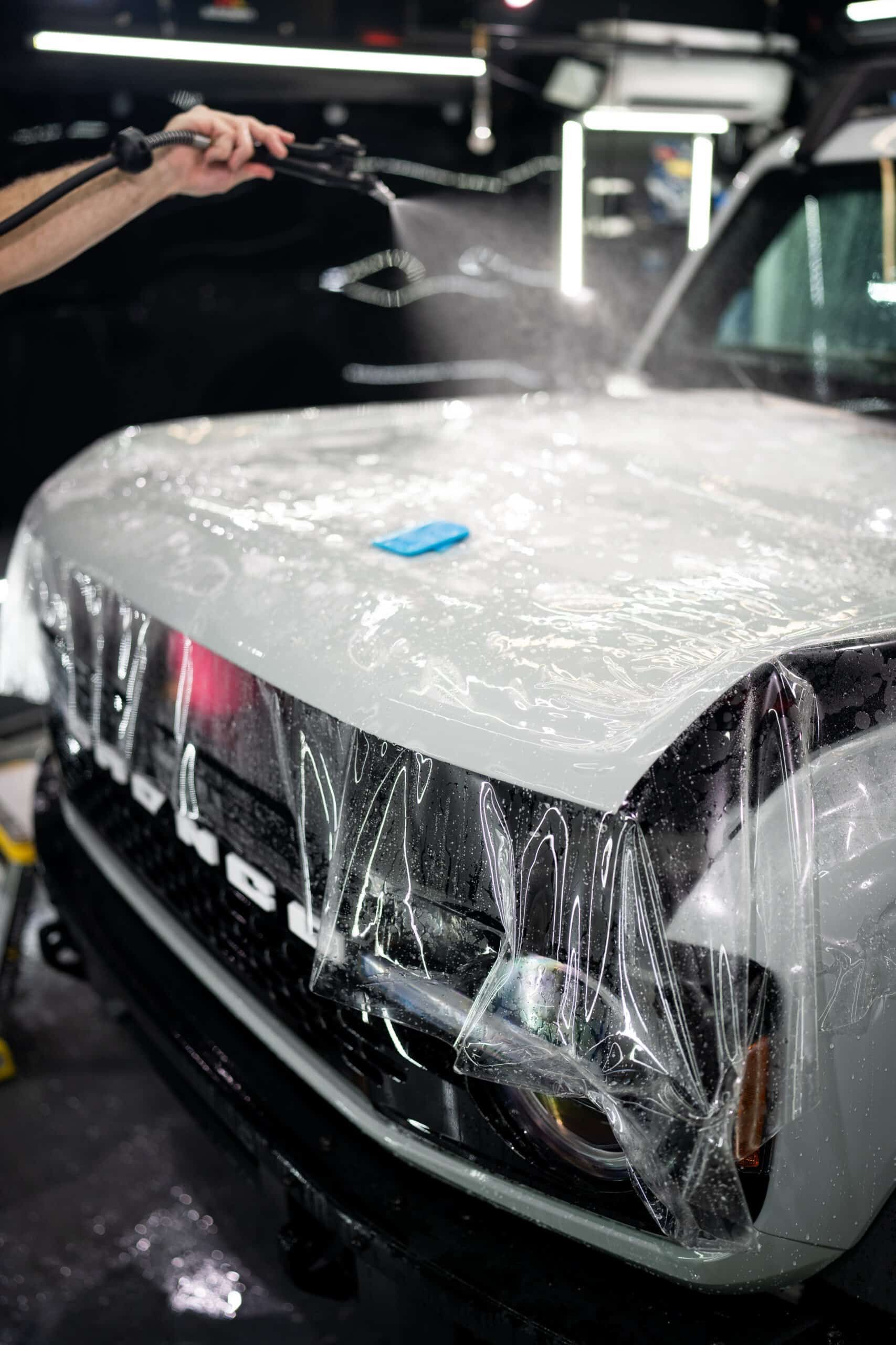 A person is spraying water on a white car.