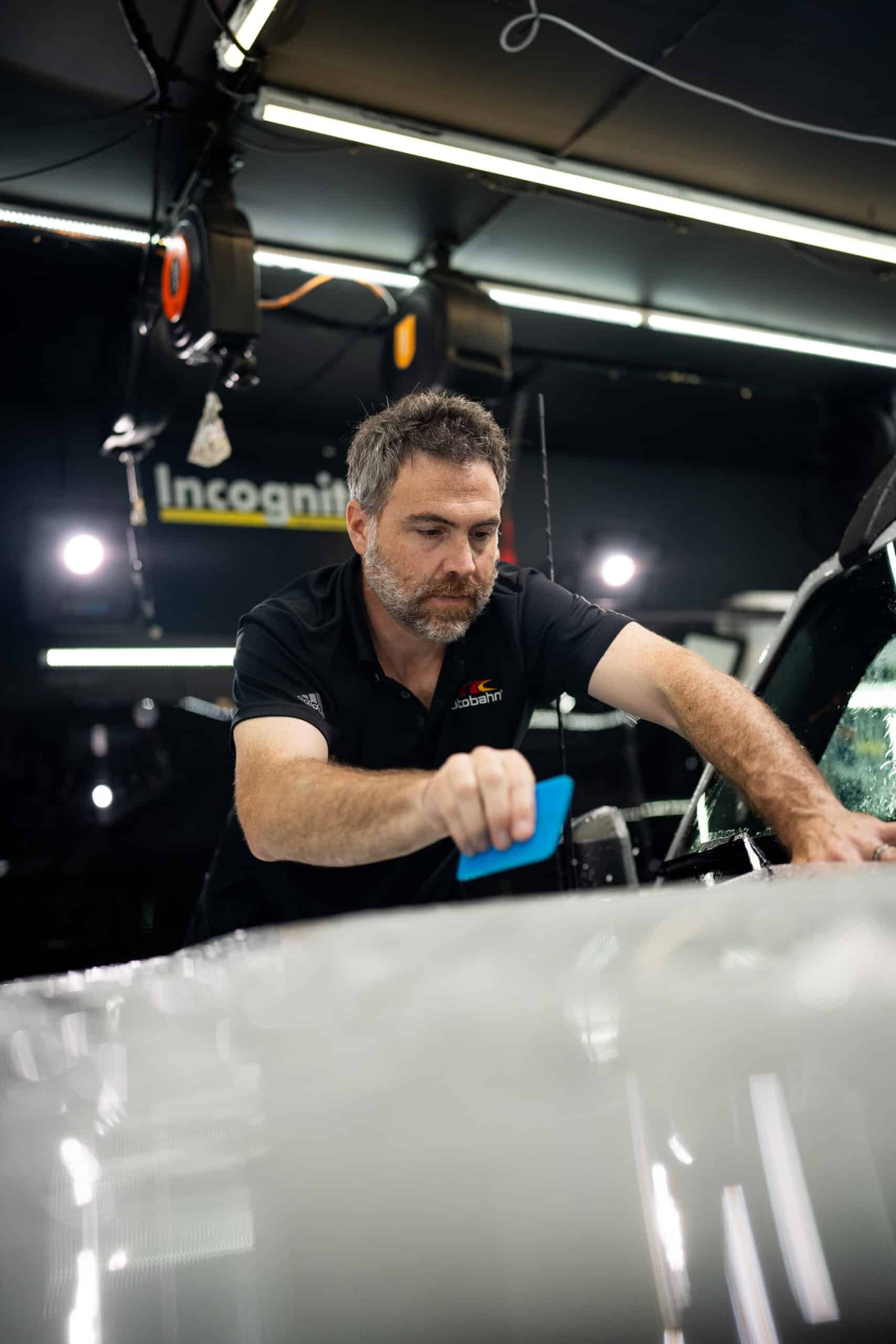 A man is wrapping a car with plastic wrap in a garage.