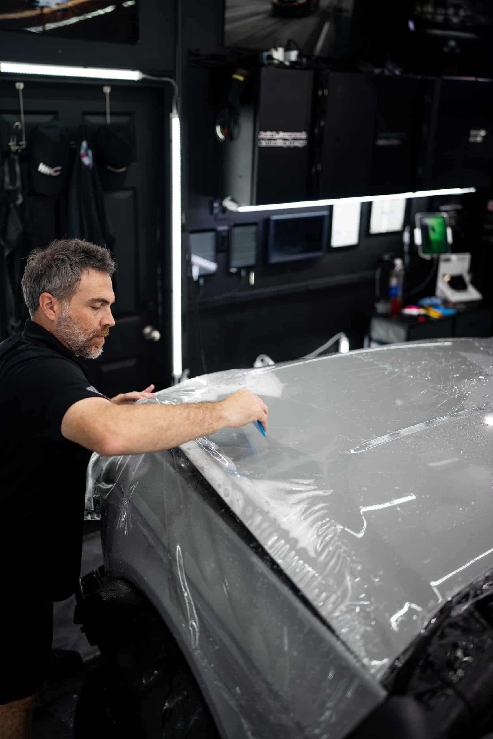A man is wrapping a car with plastic wrap in a garage.
