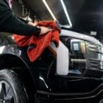 A person is cleaning a black car with a red towel.