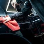 A person is cleaning the engine of a car with a towel.