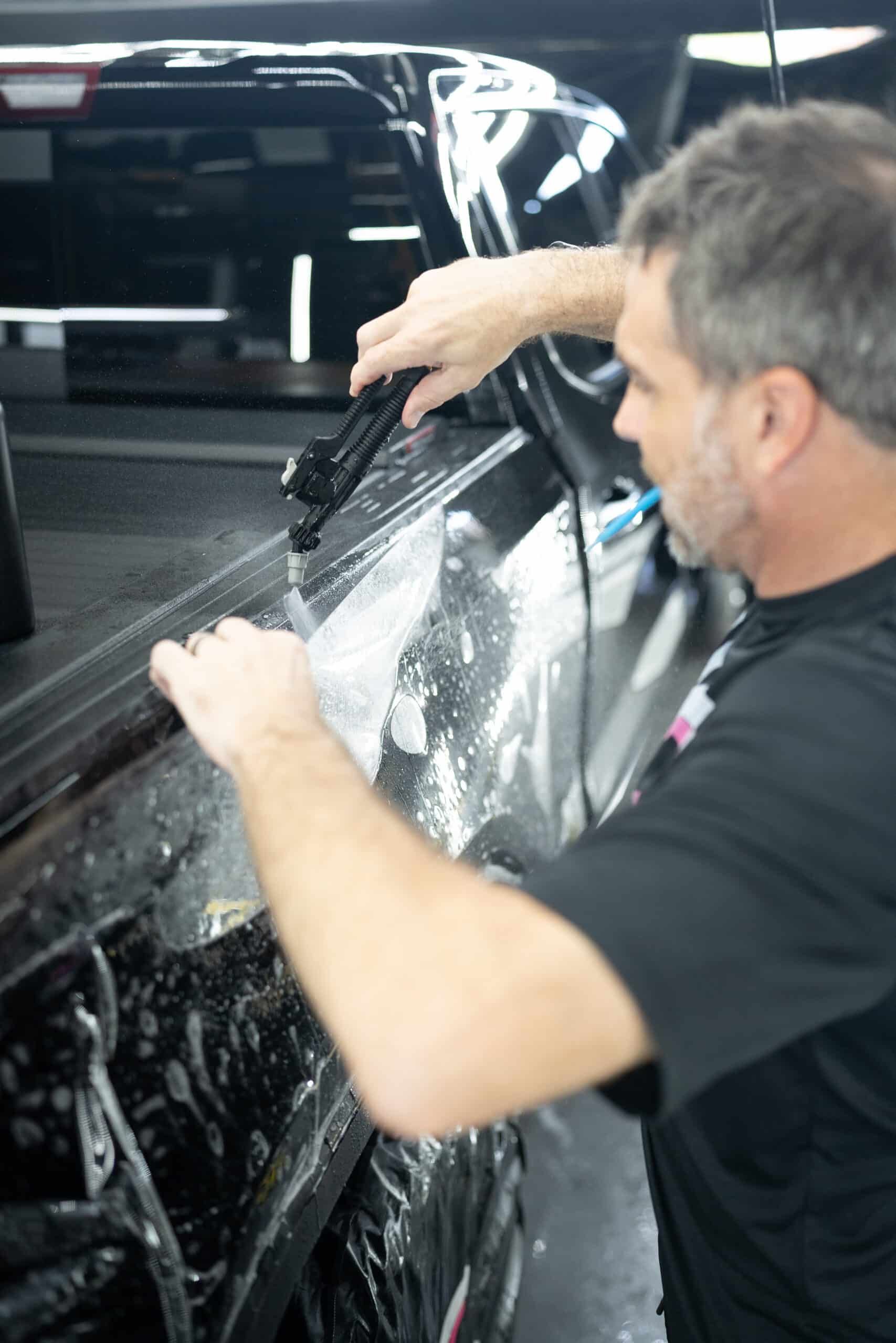 A man is applying a protective film to the side of a truck.