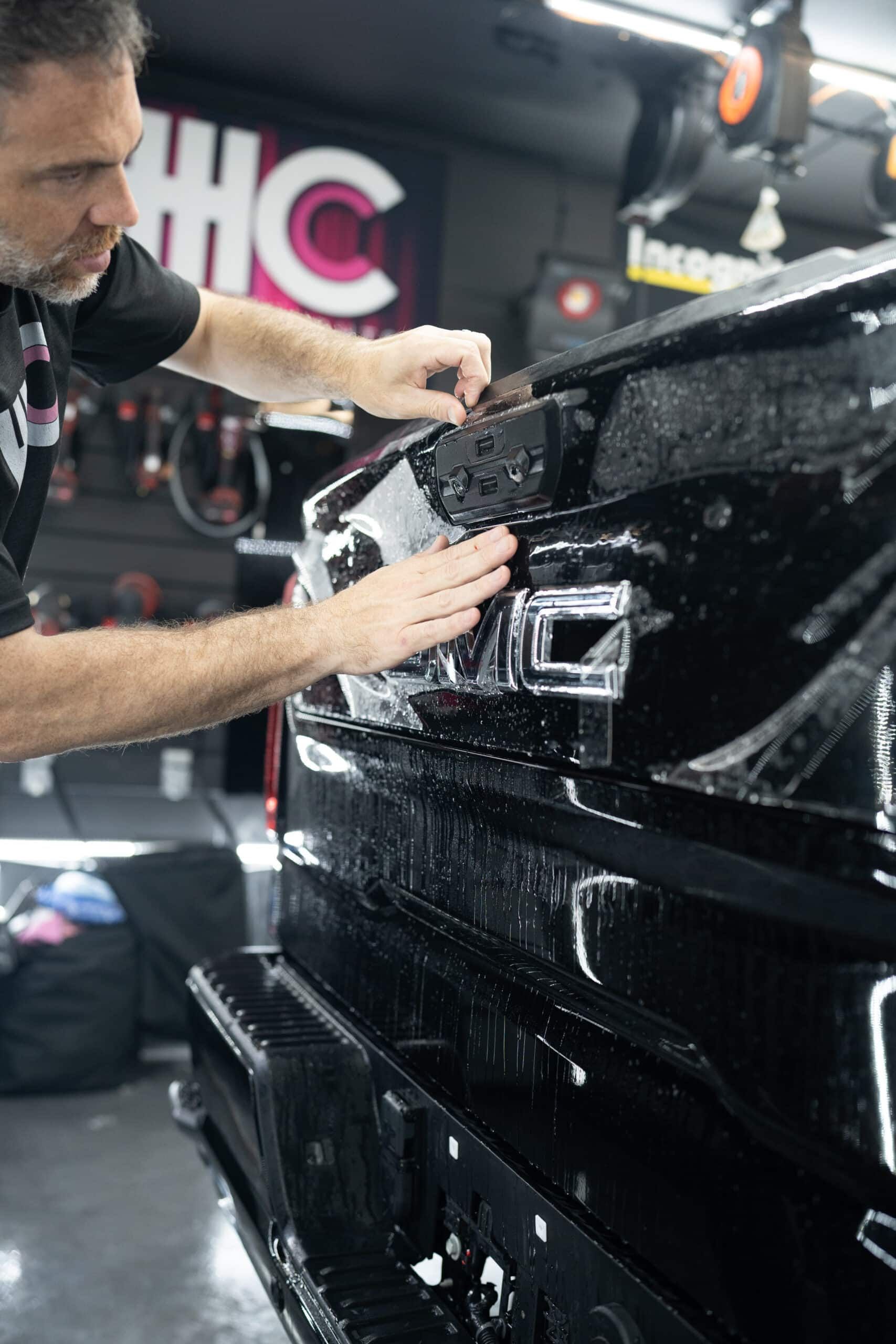 A man is applying a protective film to the back of a black truck.