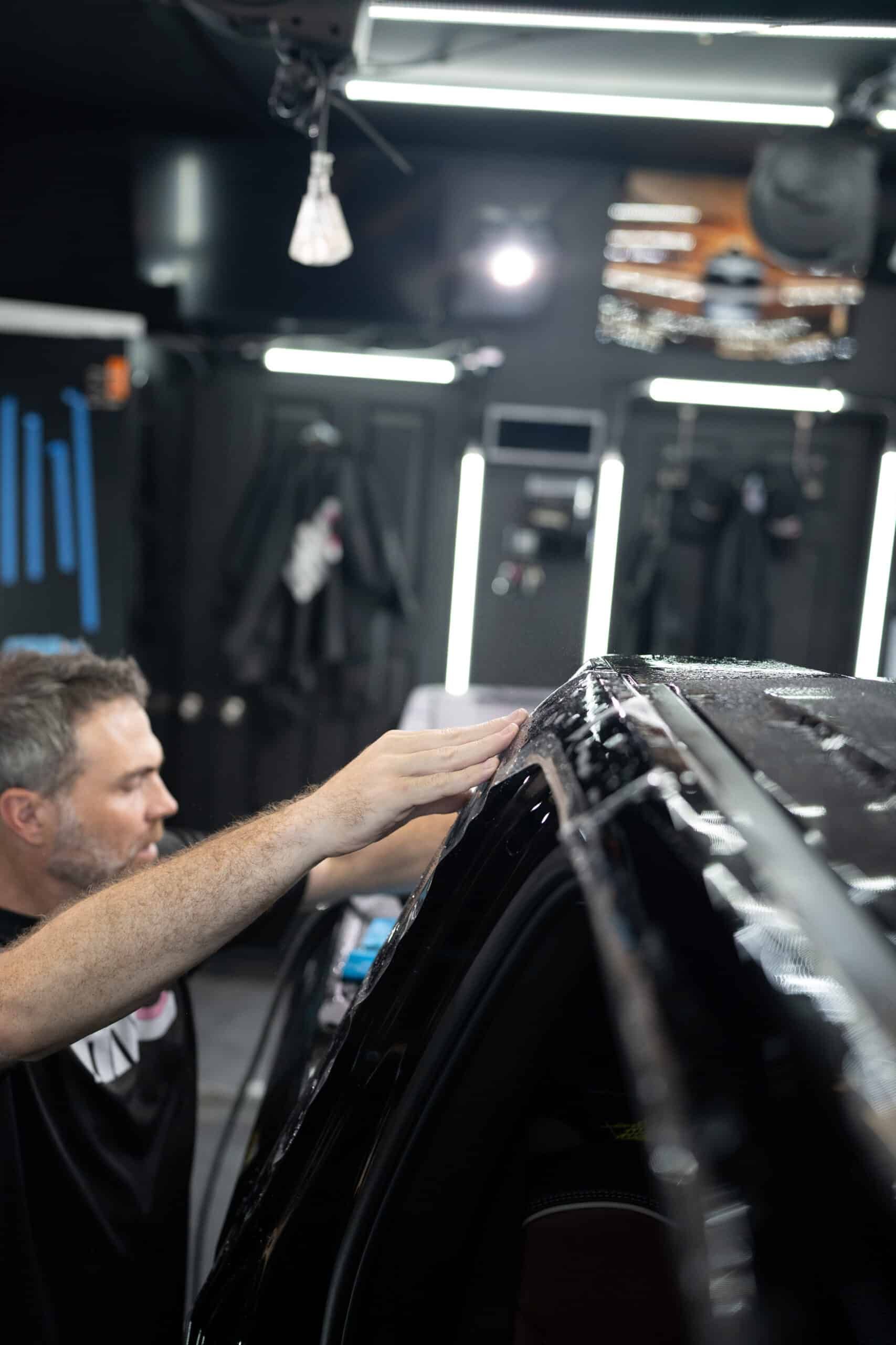 A man is working on the roof of a car in a garage.