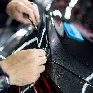 A person is applying a protective film to the back of a car.