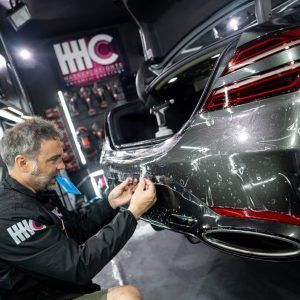 A man is applying a protective film to the back of a car.