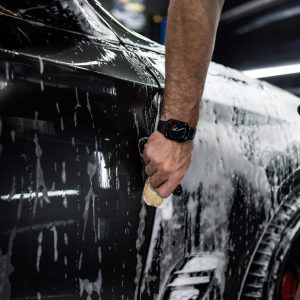 A man is washing a car with a sponge and foam.