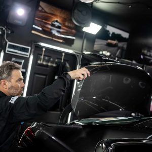 A man is working on a black car in a garage.