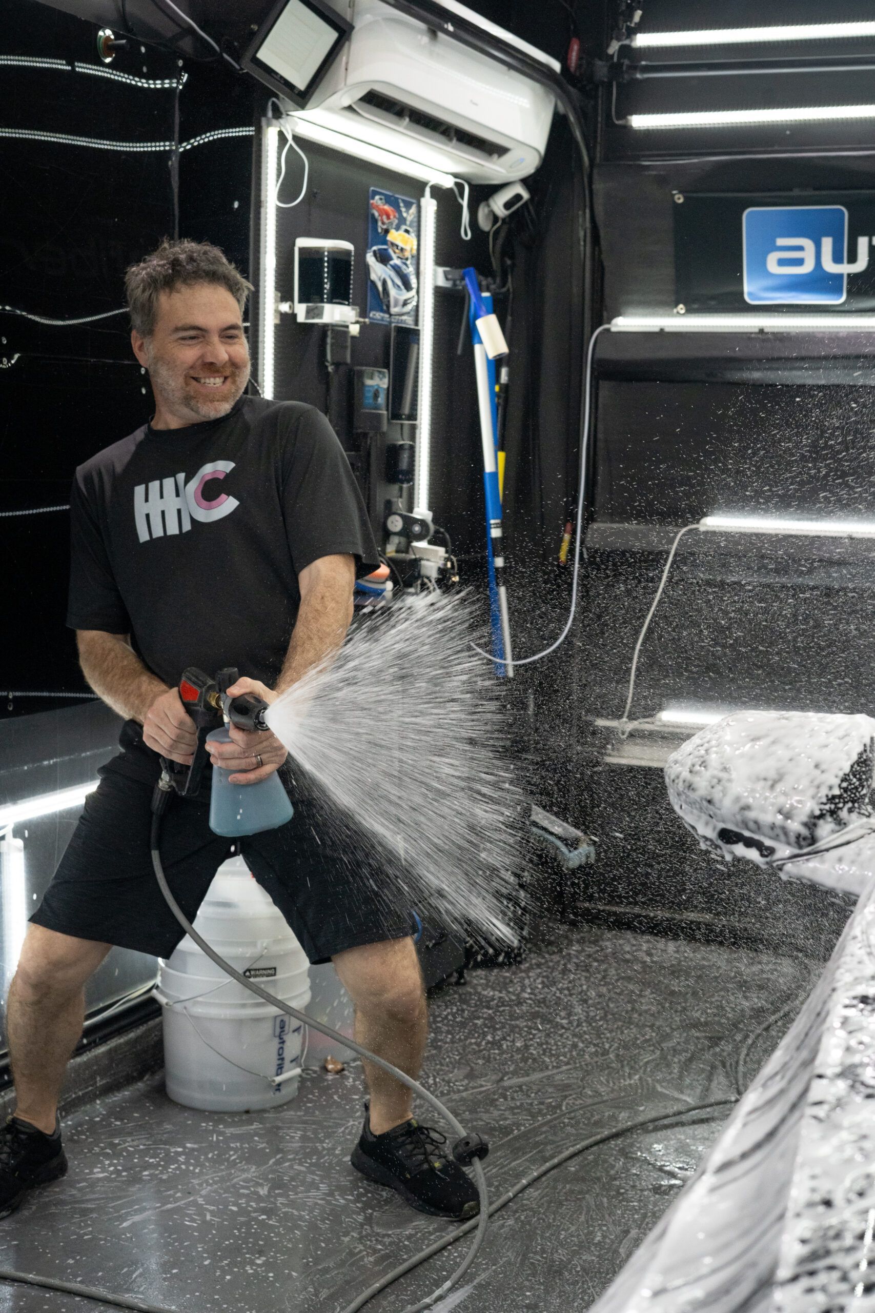 A man is spraying foam on a car in a garage.