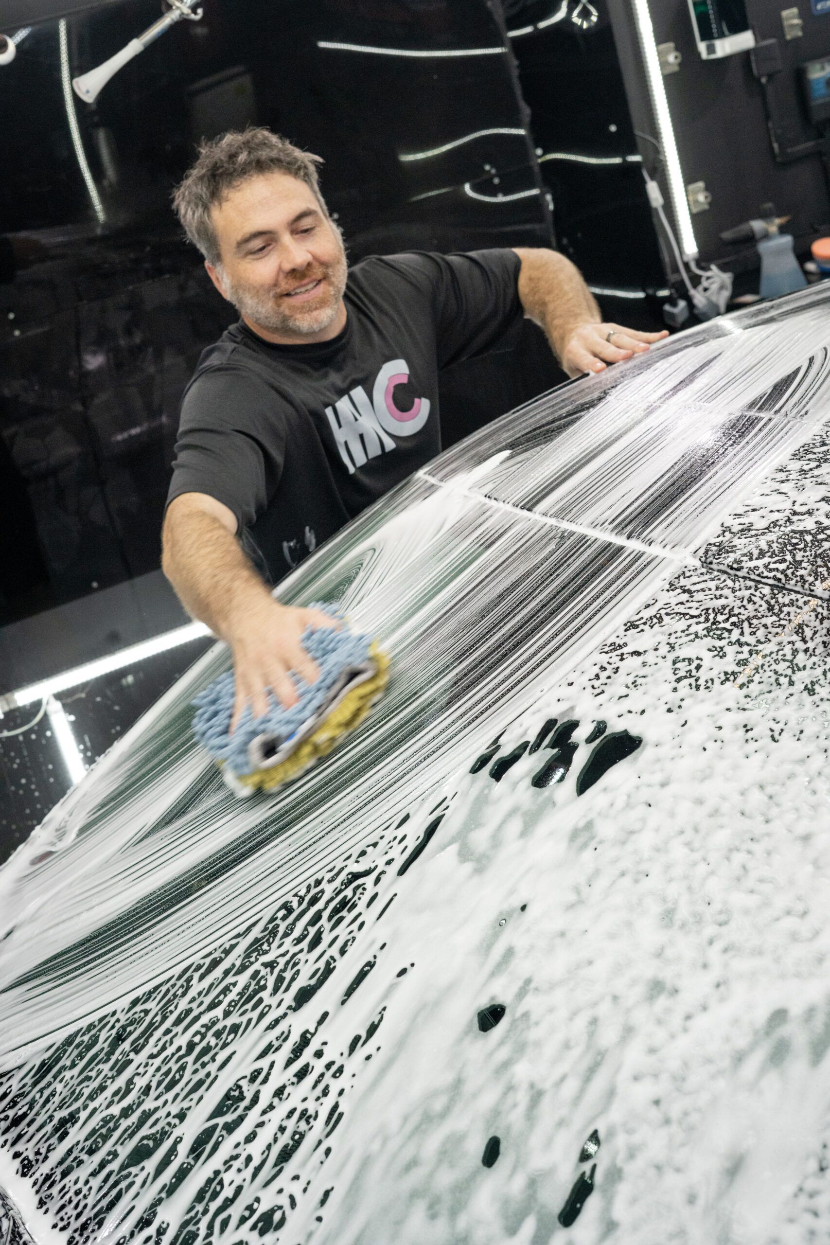 A man is washing a car with a sponge and foam.