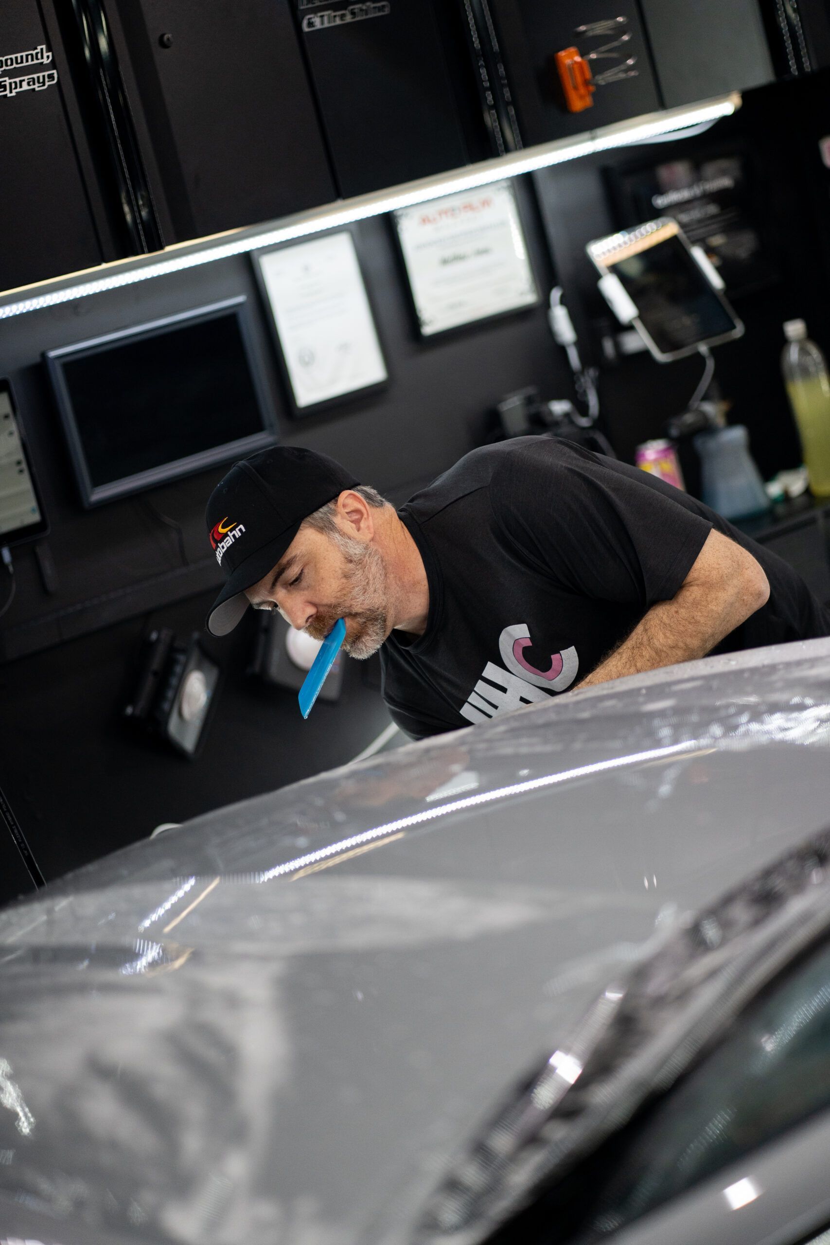 A man is wrapping the hood of a car in plastic.