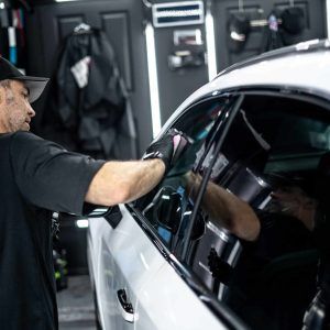 A man is cleaning the windows of a white car in a garage.