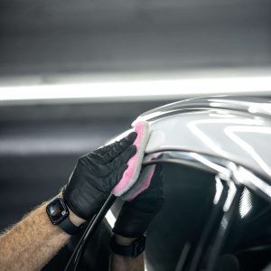 A person is cleaning a car with a pink sponge.