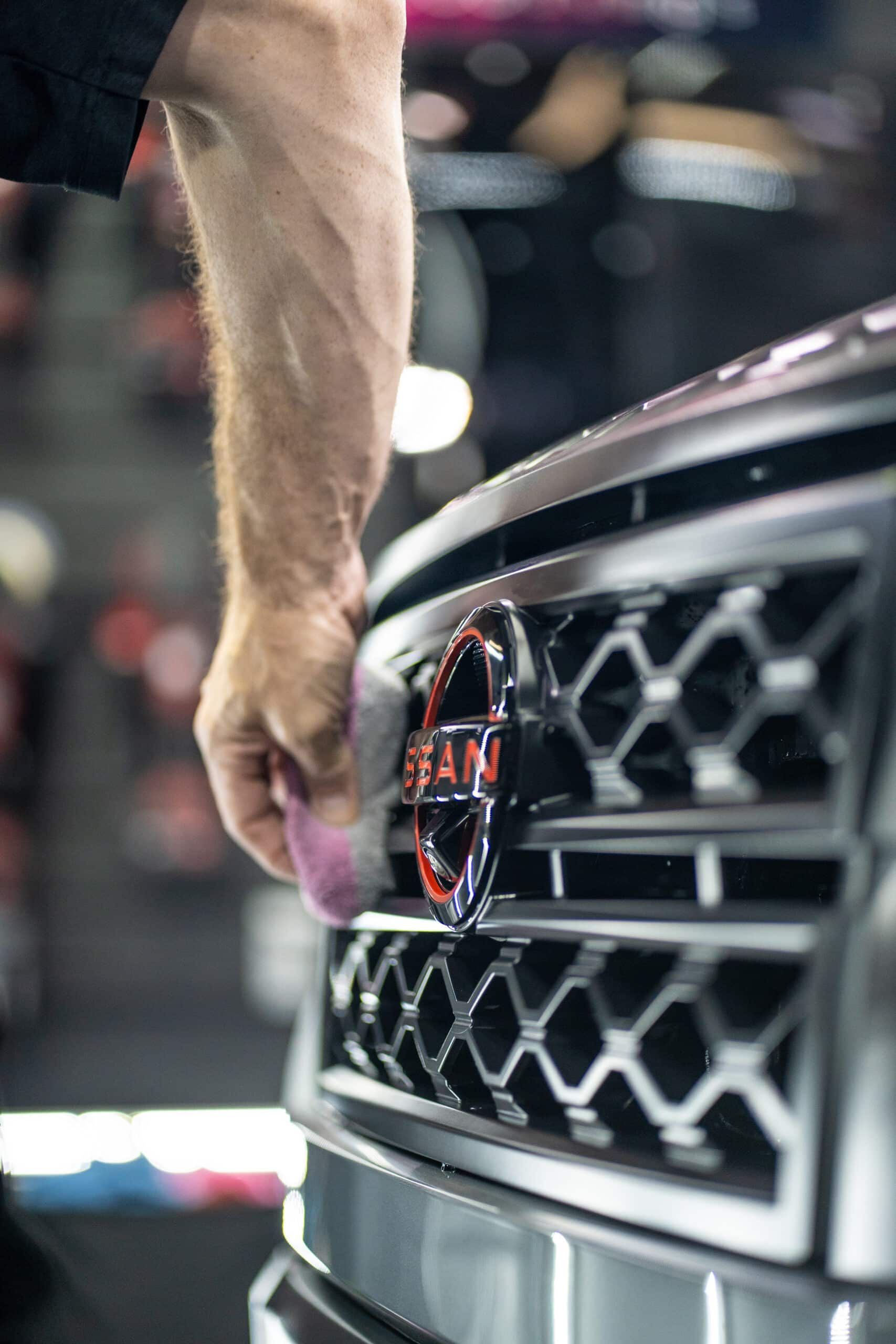 A man is cleaning the front grille of a nissan truck.