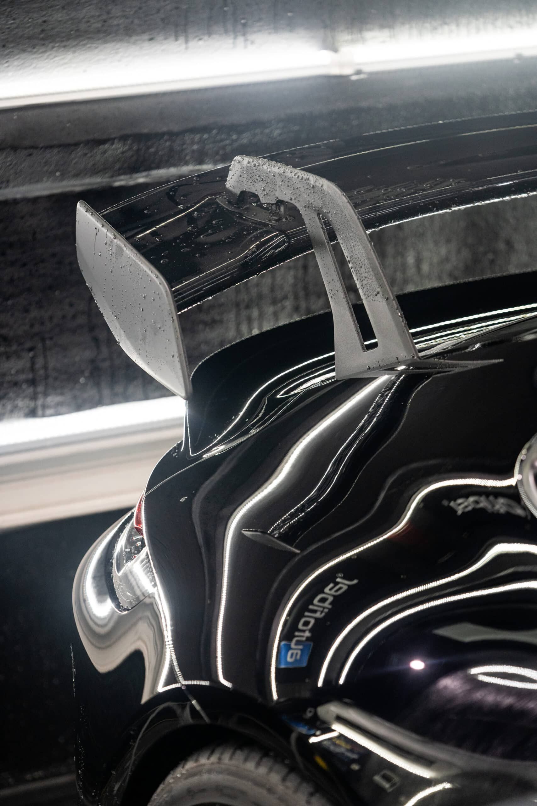 A black car with a spoiler on the back is parked in a garage.