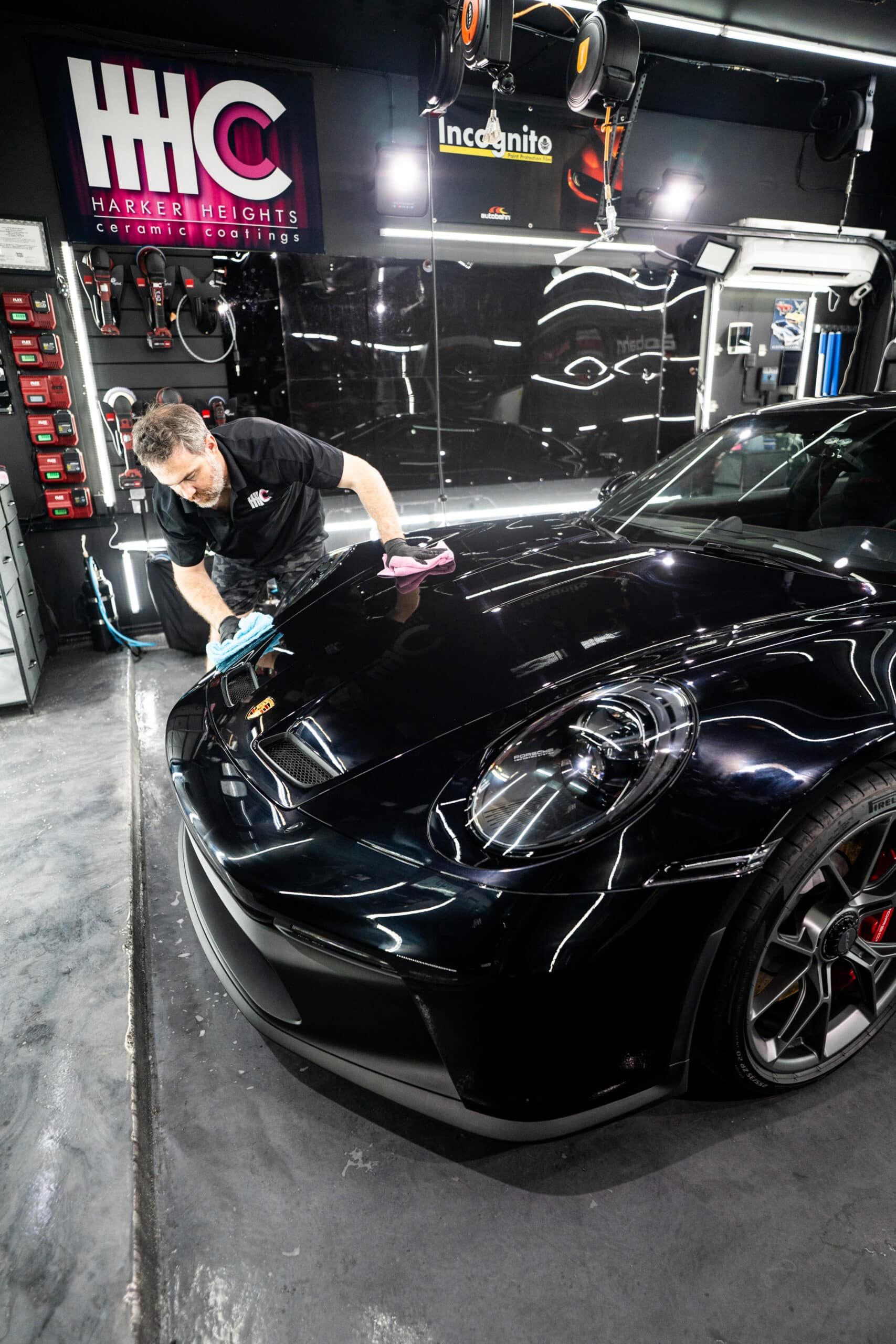 A man is polishing a black car in a garage.