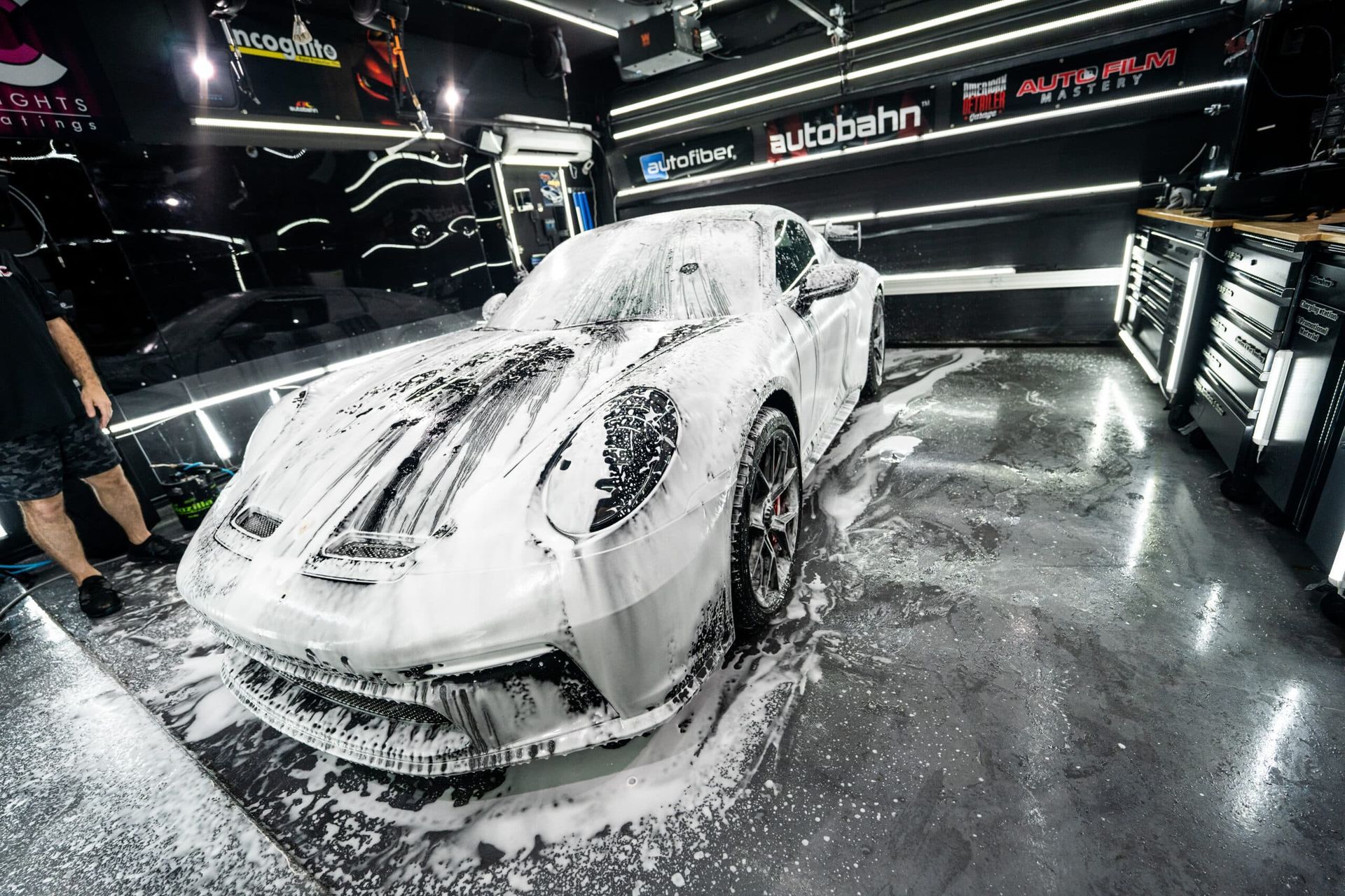 A white sports car is covered in foam in a garage.