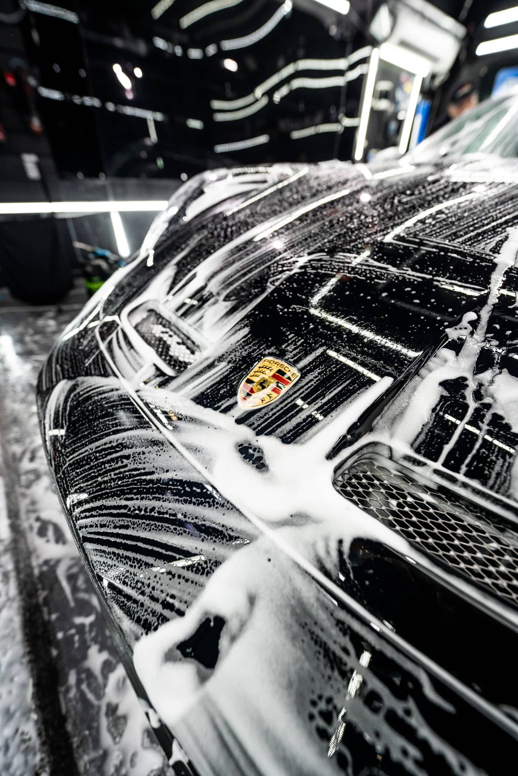 A black car is being washed with soap and water in a car wash.