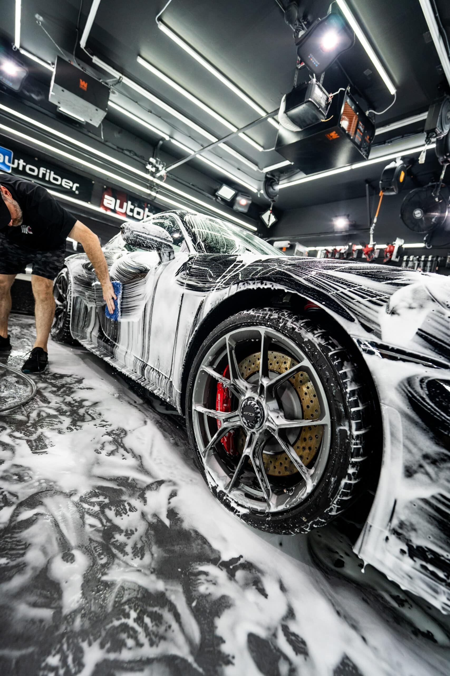 A man is washing a sports car in a garage.