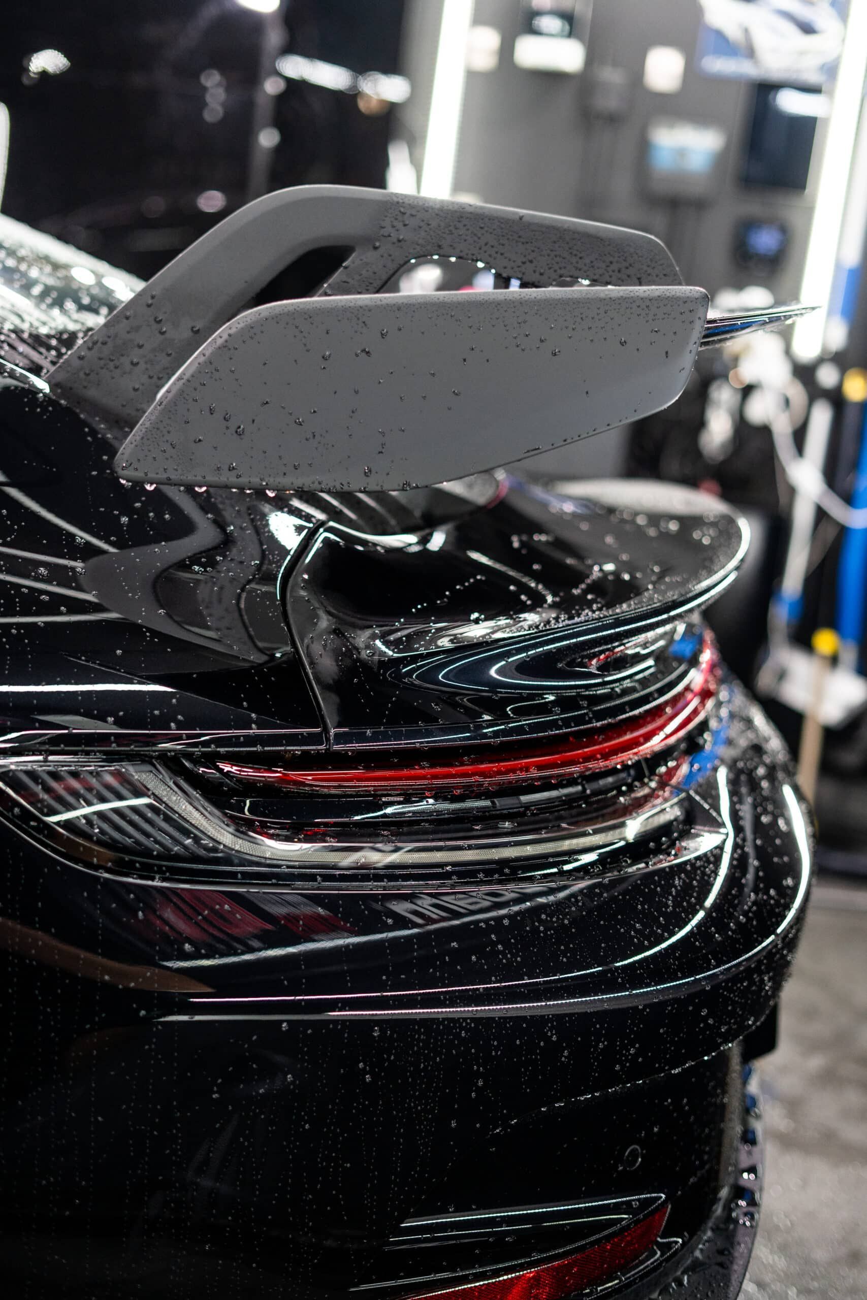 A black car with a spoiler on the back is sitting in a garage.