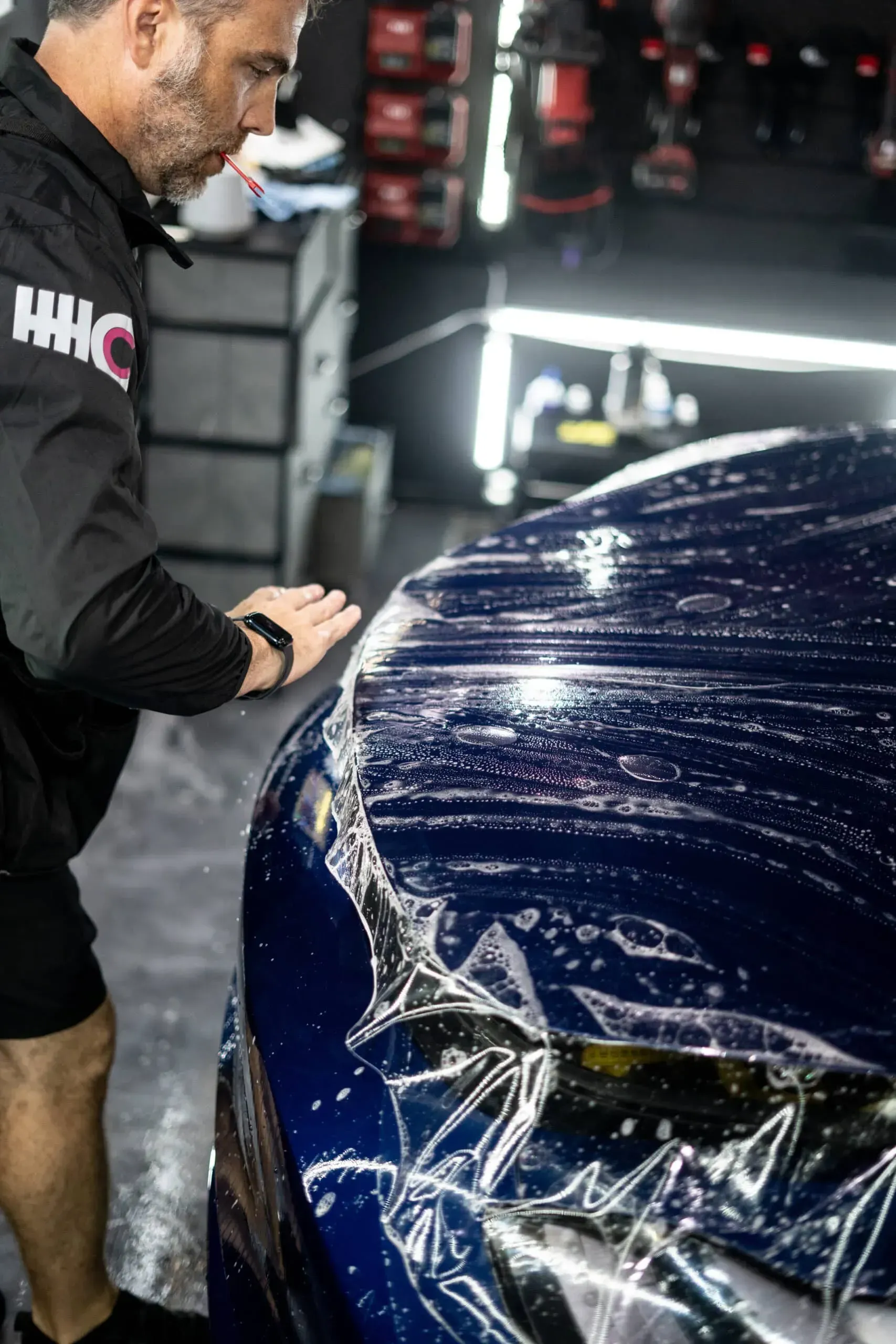 A man is wrapping a blue car with plastic wrap.