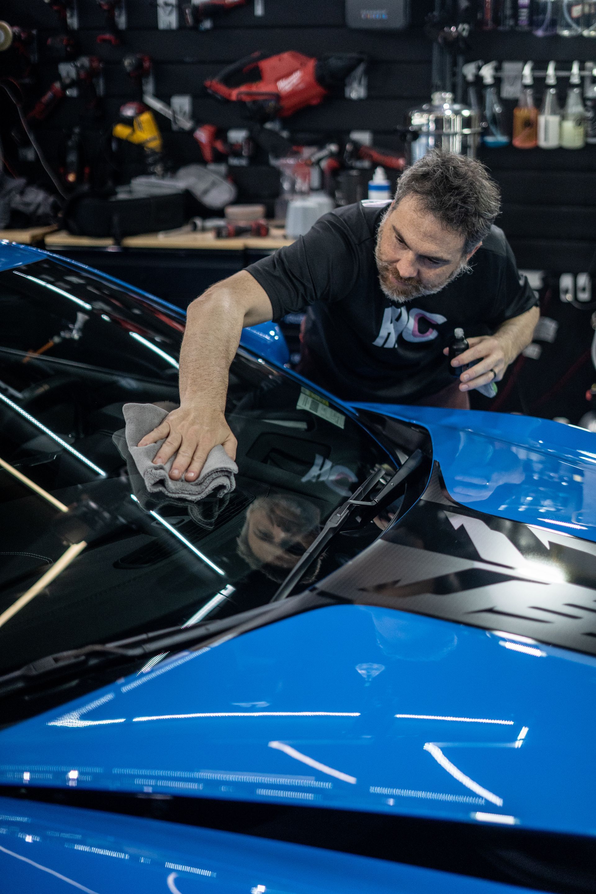 A man is cleaning the windshield of a blue car.