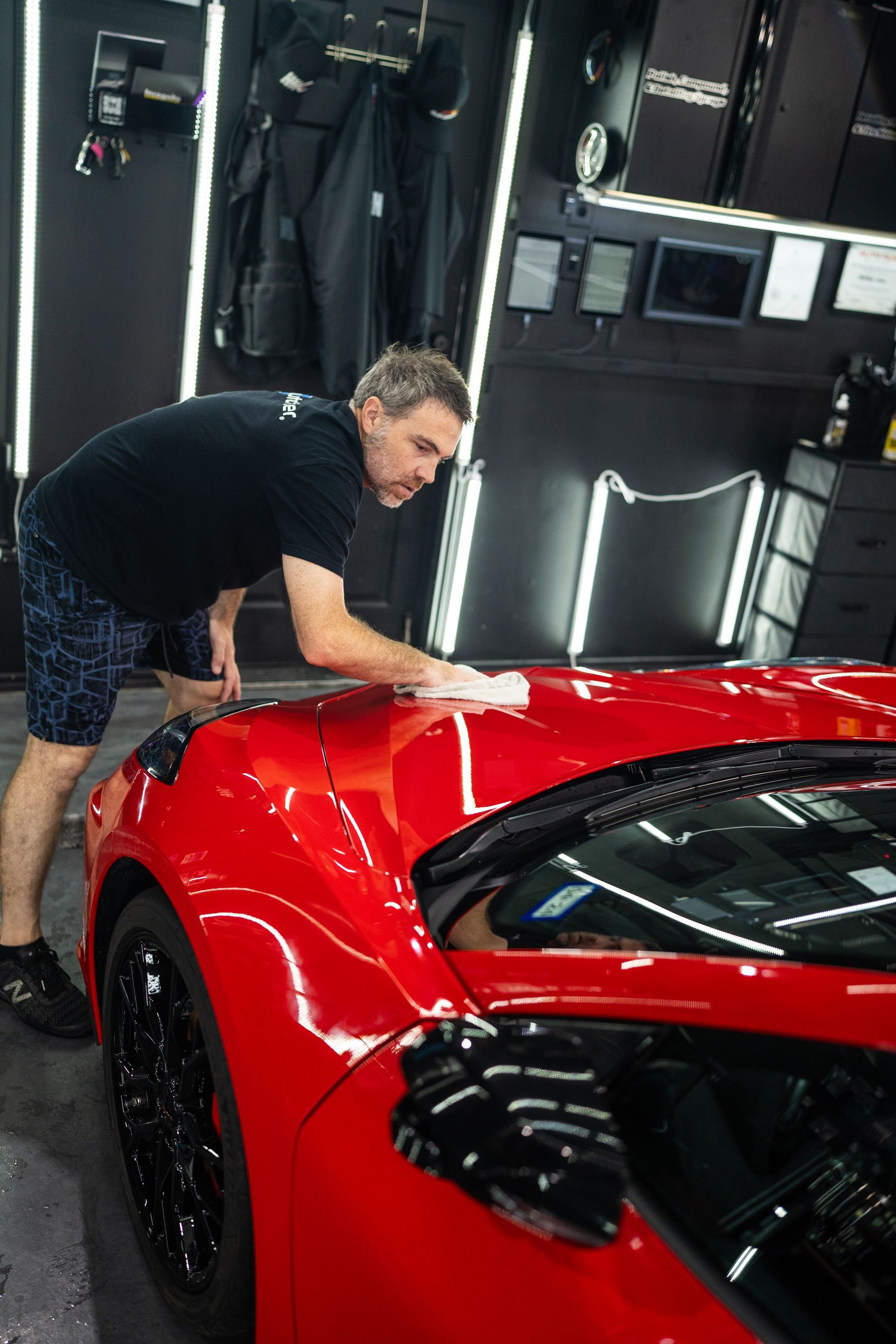 A man is cleaning a red sports car in a garage.