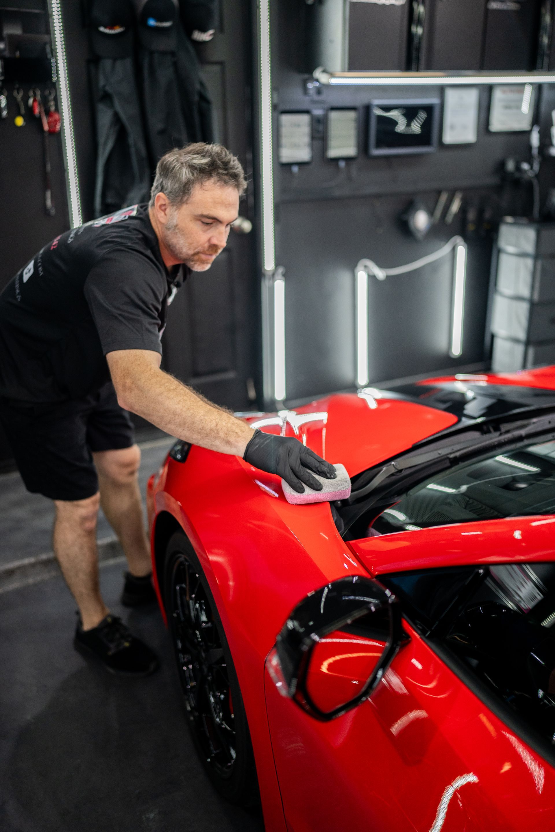 A man is polishing a red sports car in a garage.