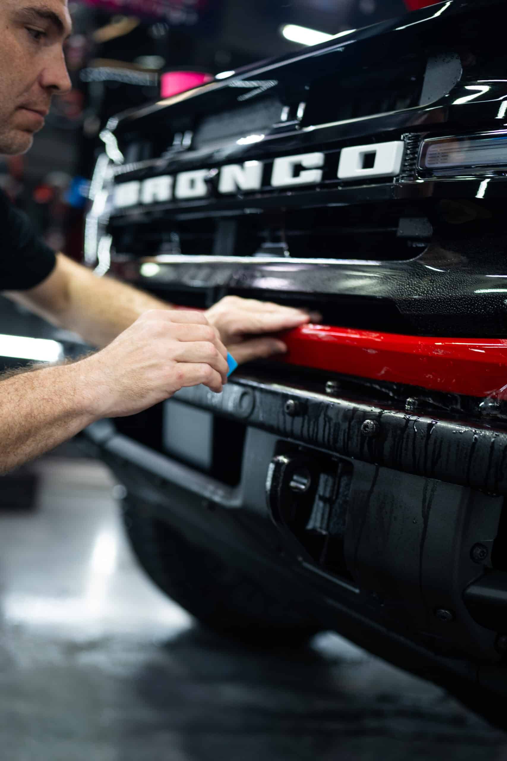 A man is working on the front of a black bronco