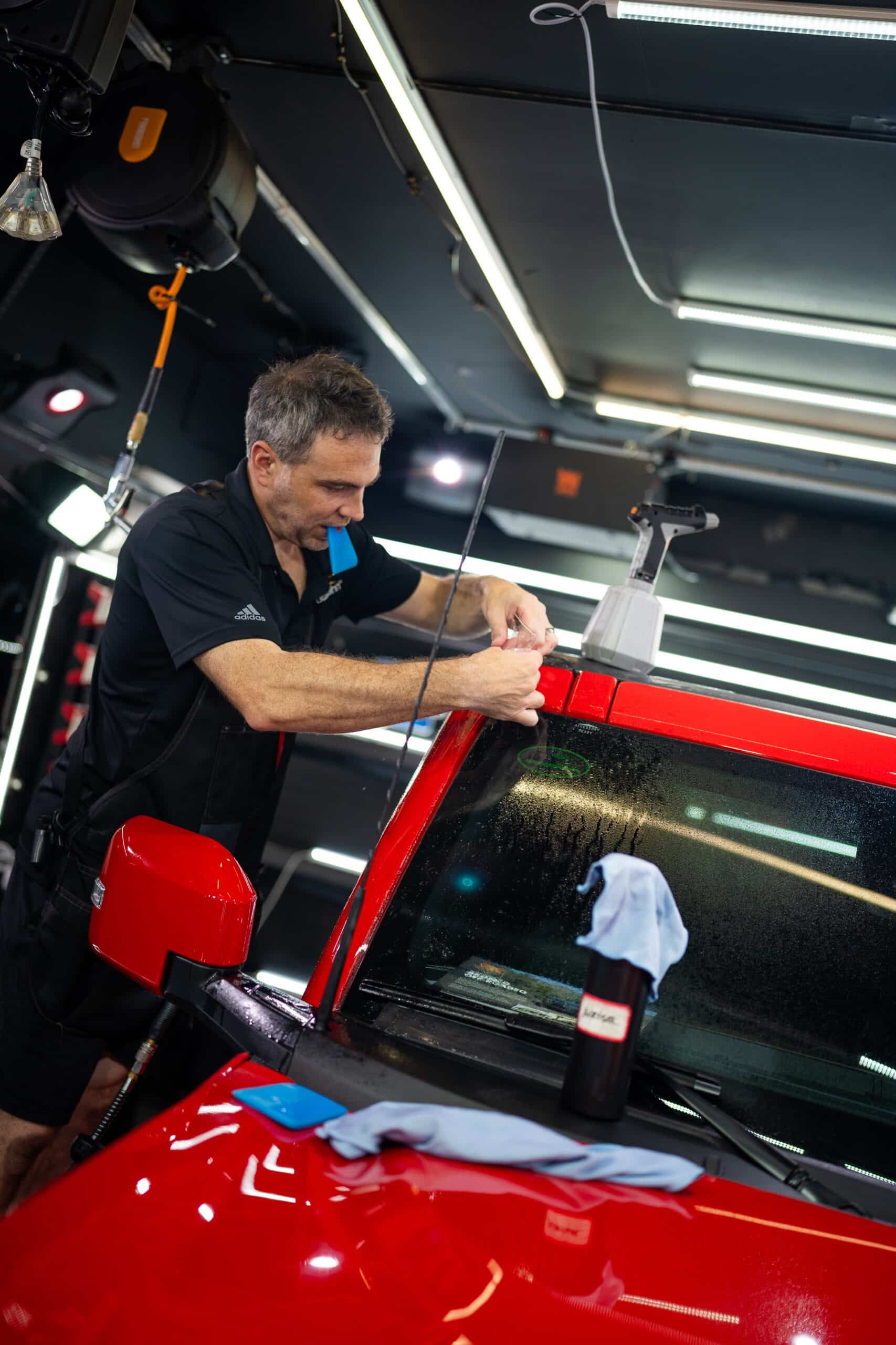 A man is working on a red car in a garage.
