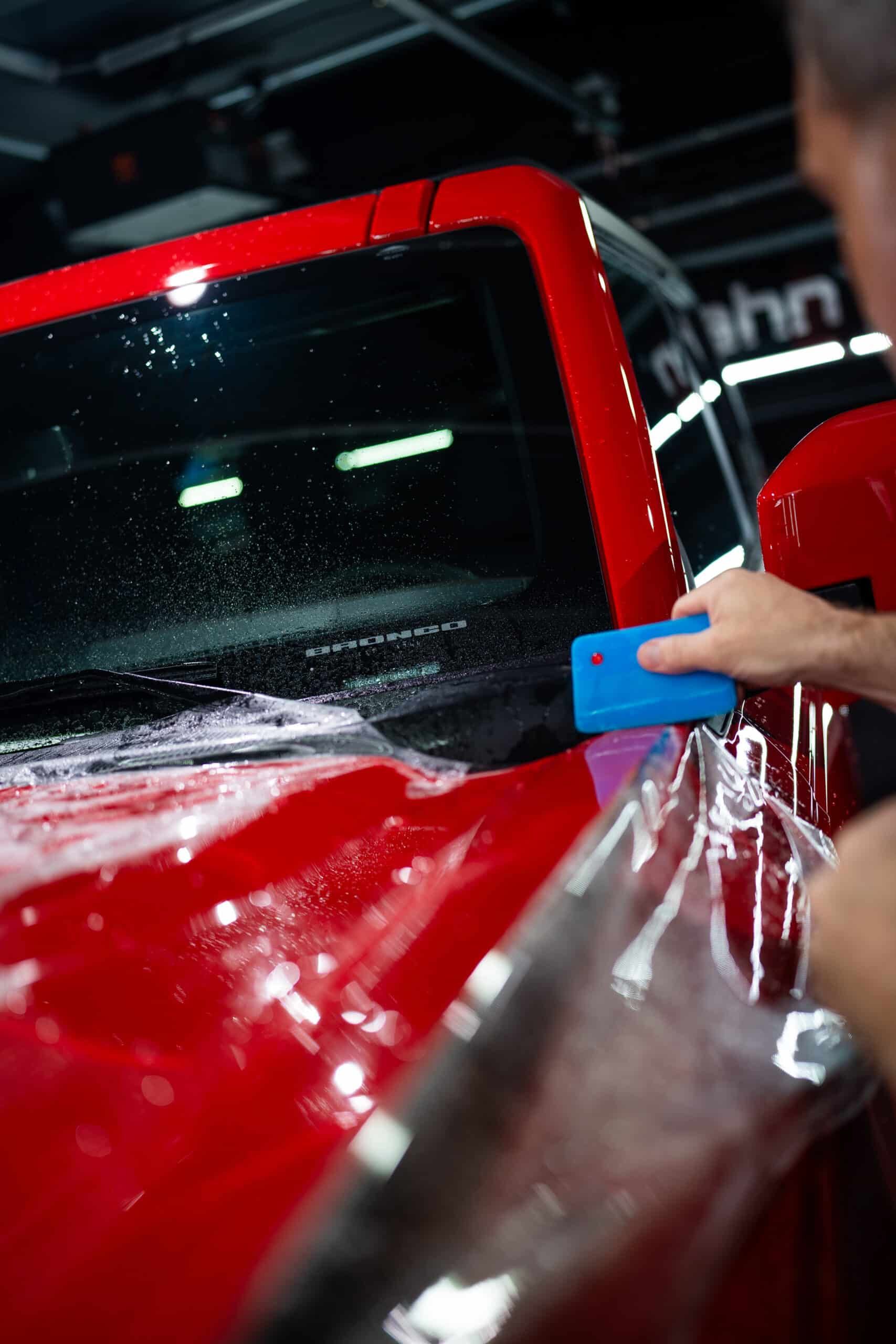 A man is wrapping a red truck with plastic wrap.