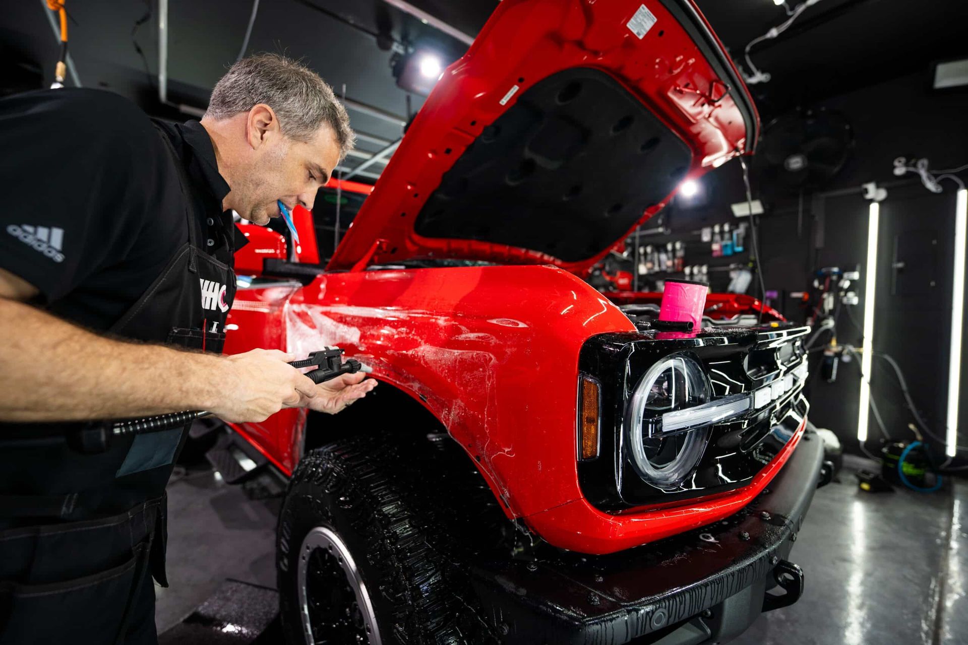 A man is working on a red truck in a garage with the hood open.