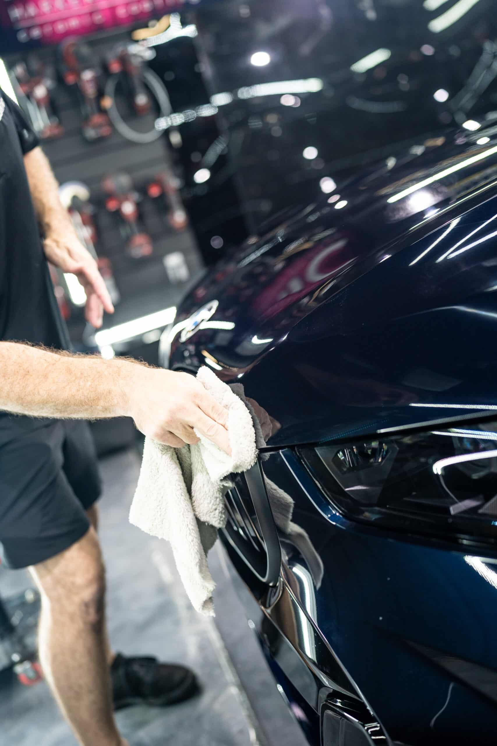 A man is cleaning a car with a towel in a garage.
