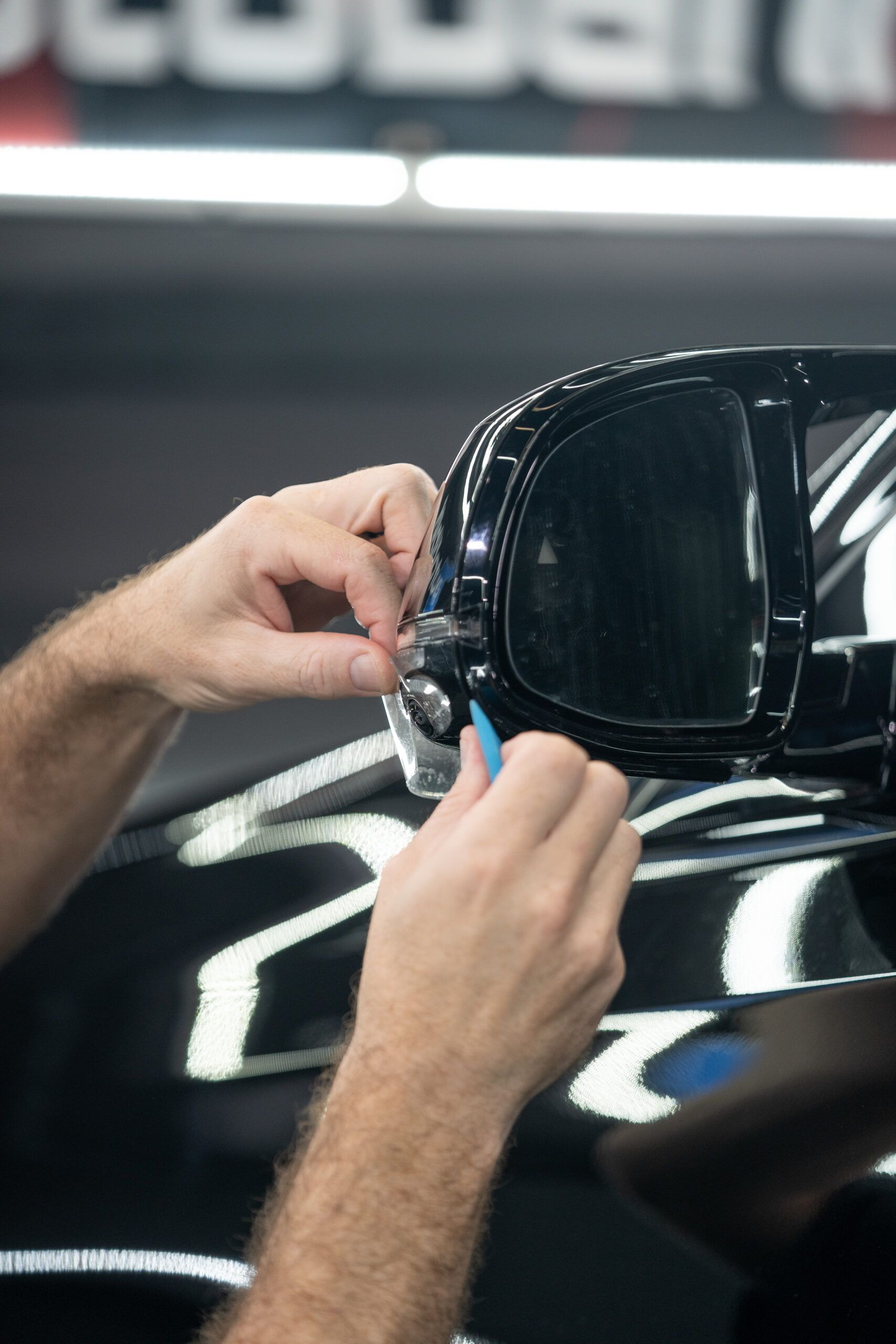 A man is fixing a side view mirror on a black car.