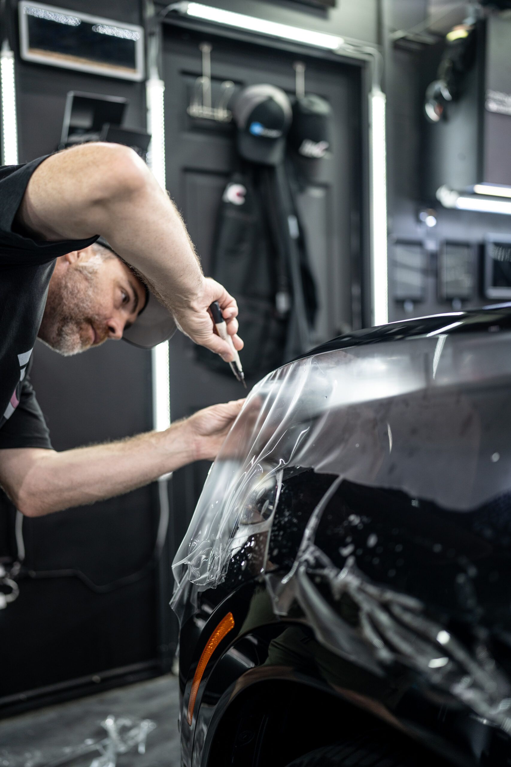 A man is wrapping a car with plastic wrap in a garage.