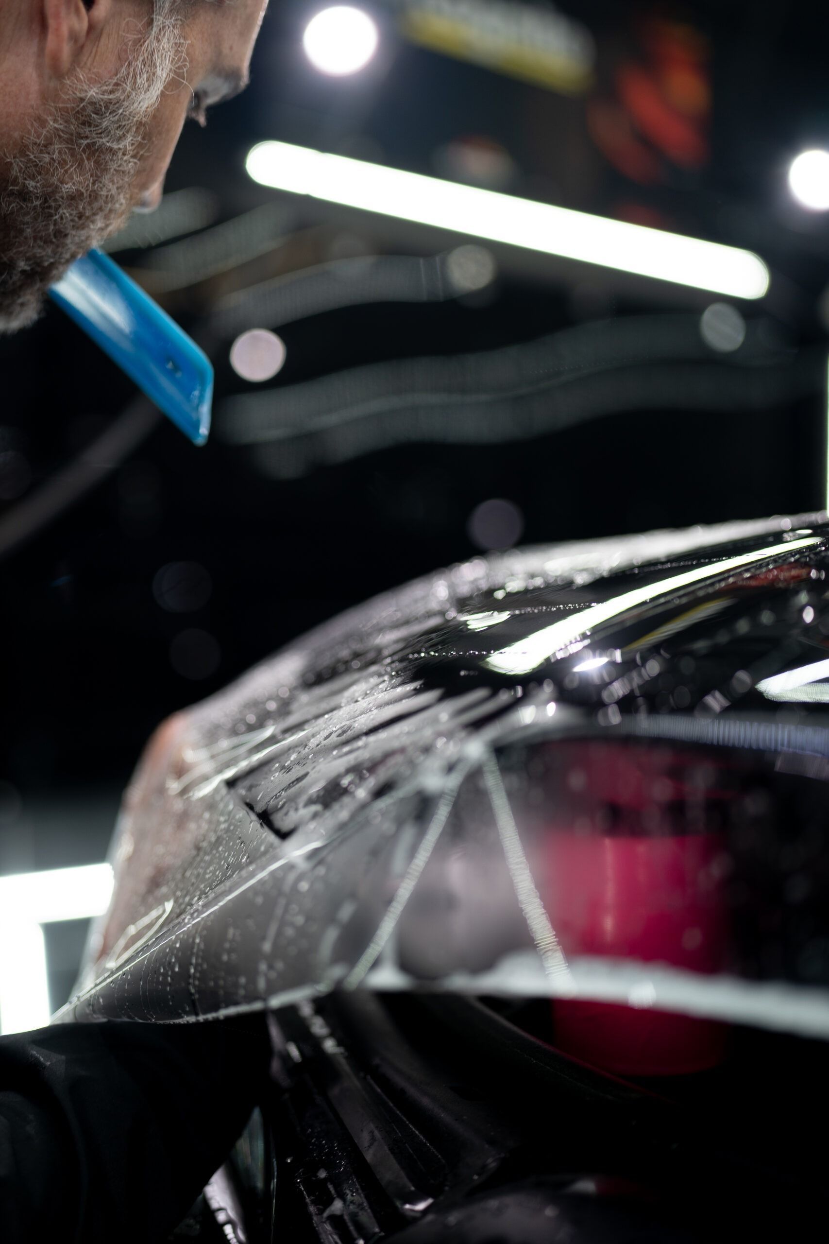 A man is applying a protective film to the windshield of a car.