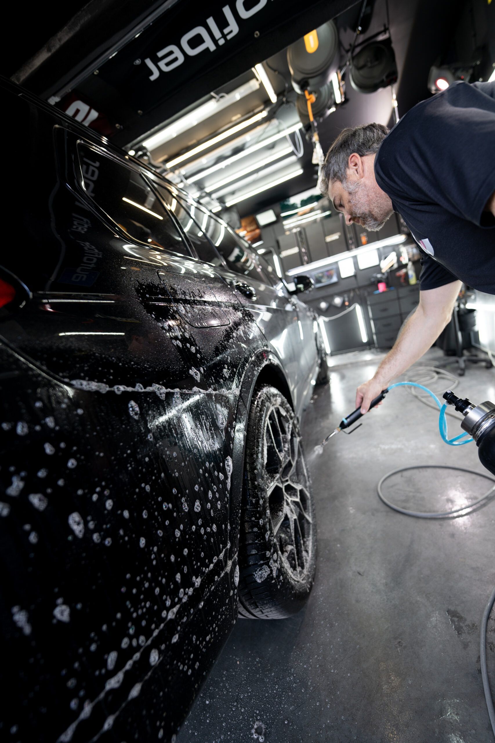 A man is washing a black car in a garage.