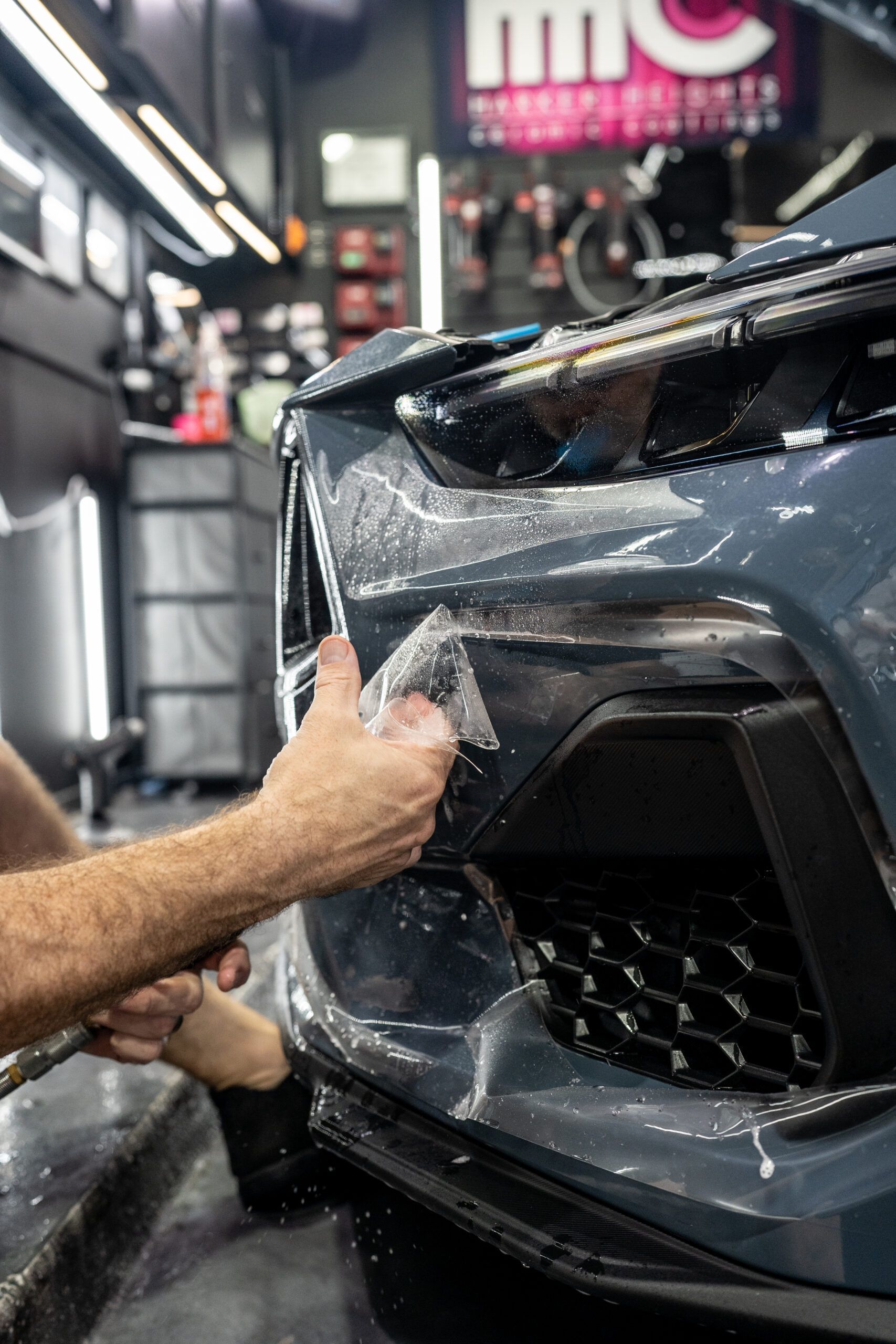 A person is applying a protective film to the front of a car.