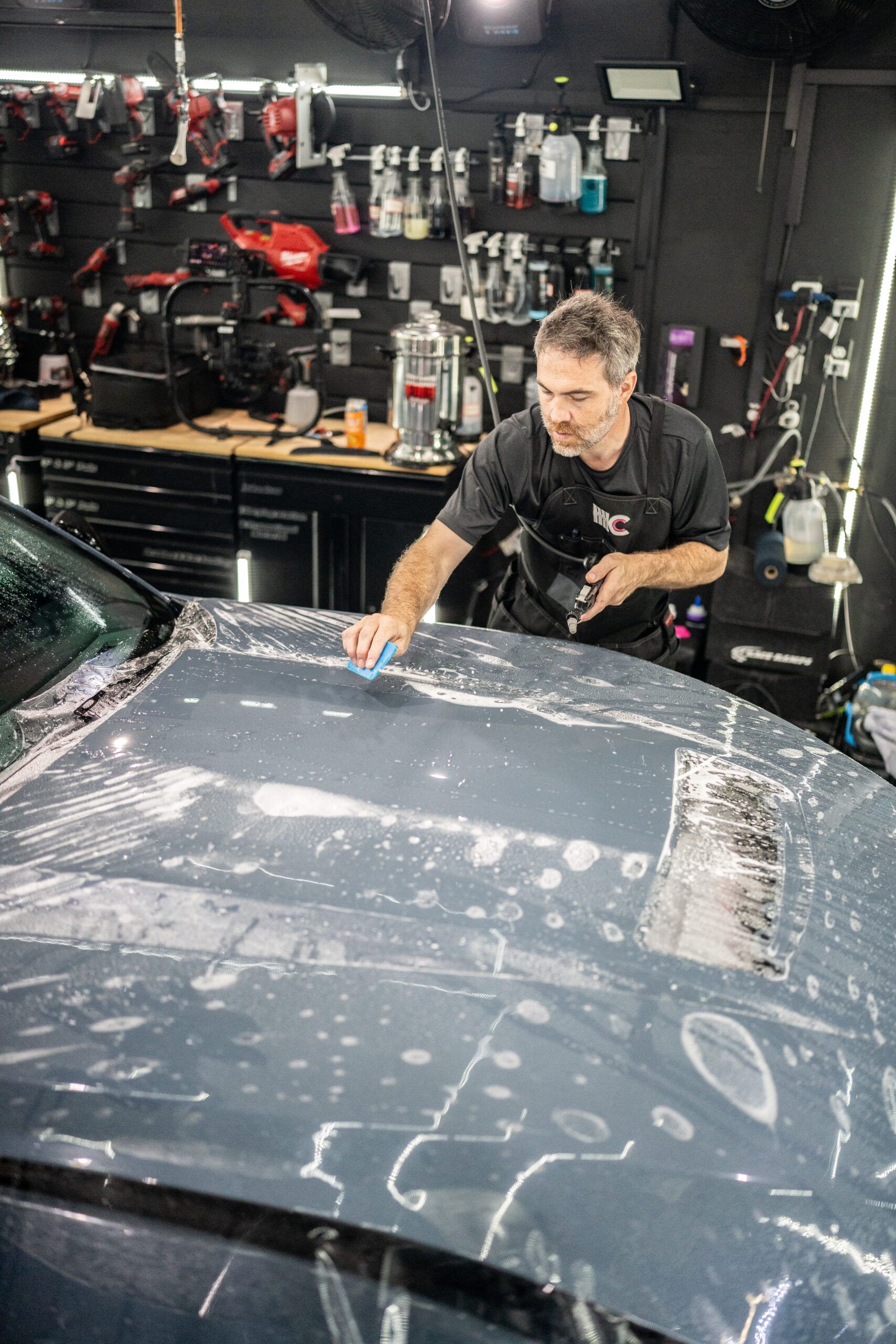 A man is polishing the hood of a car in a garage.