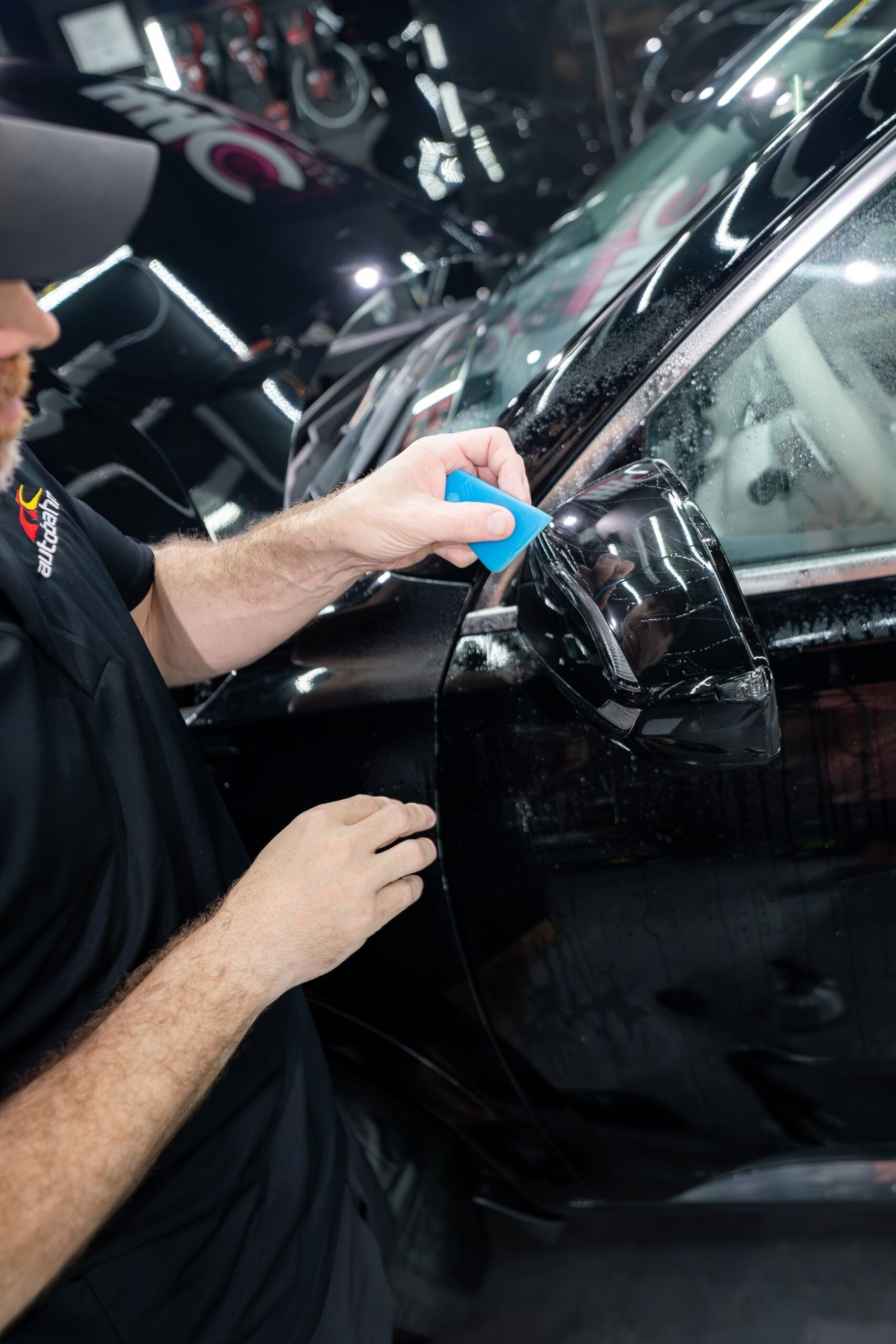 A man is applying a film to the side of a black car.