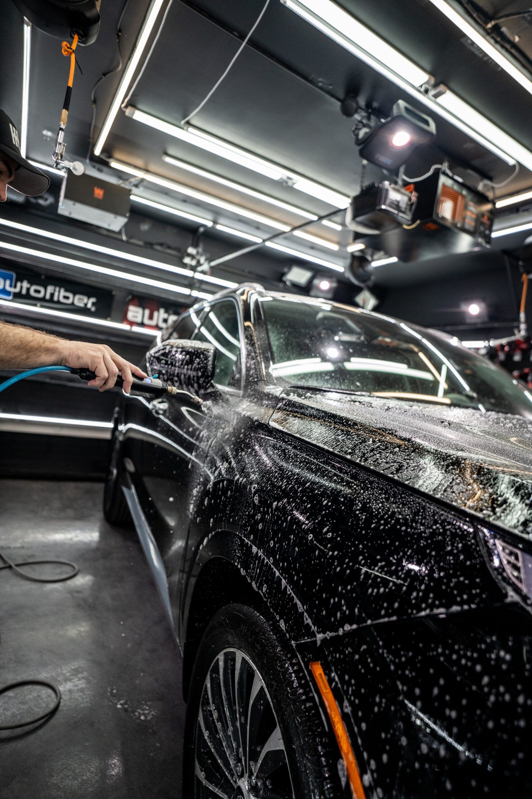 A man is washing a black car in a garage.