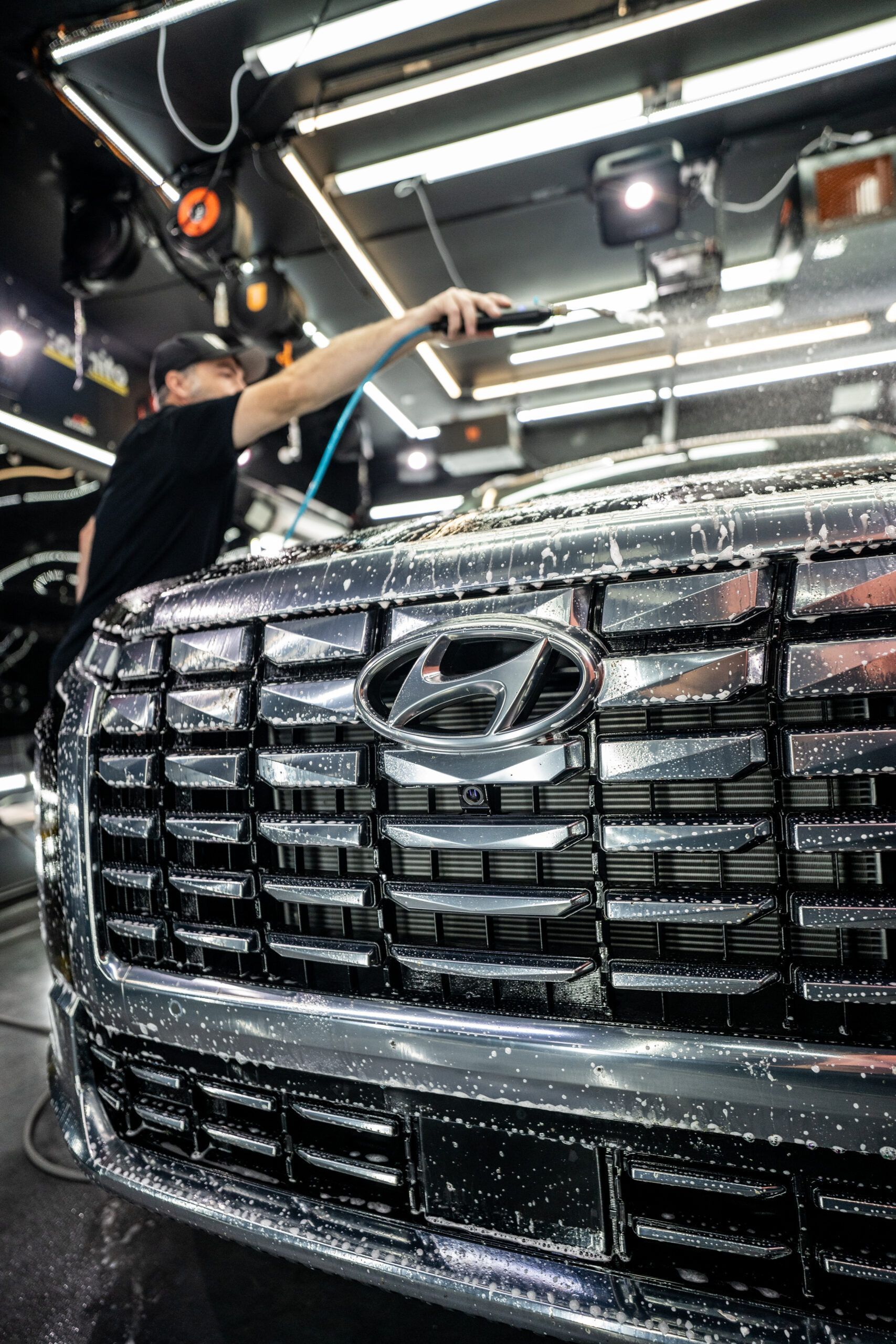A man is cleaning the front of a hyundai car in a garage.