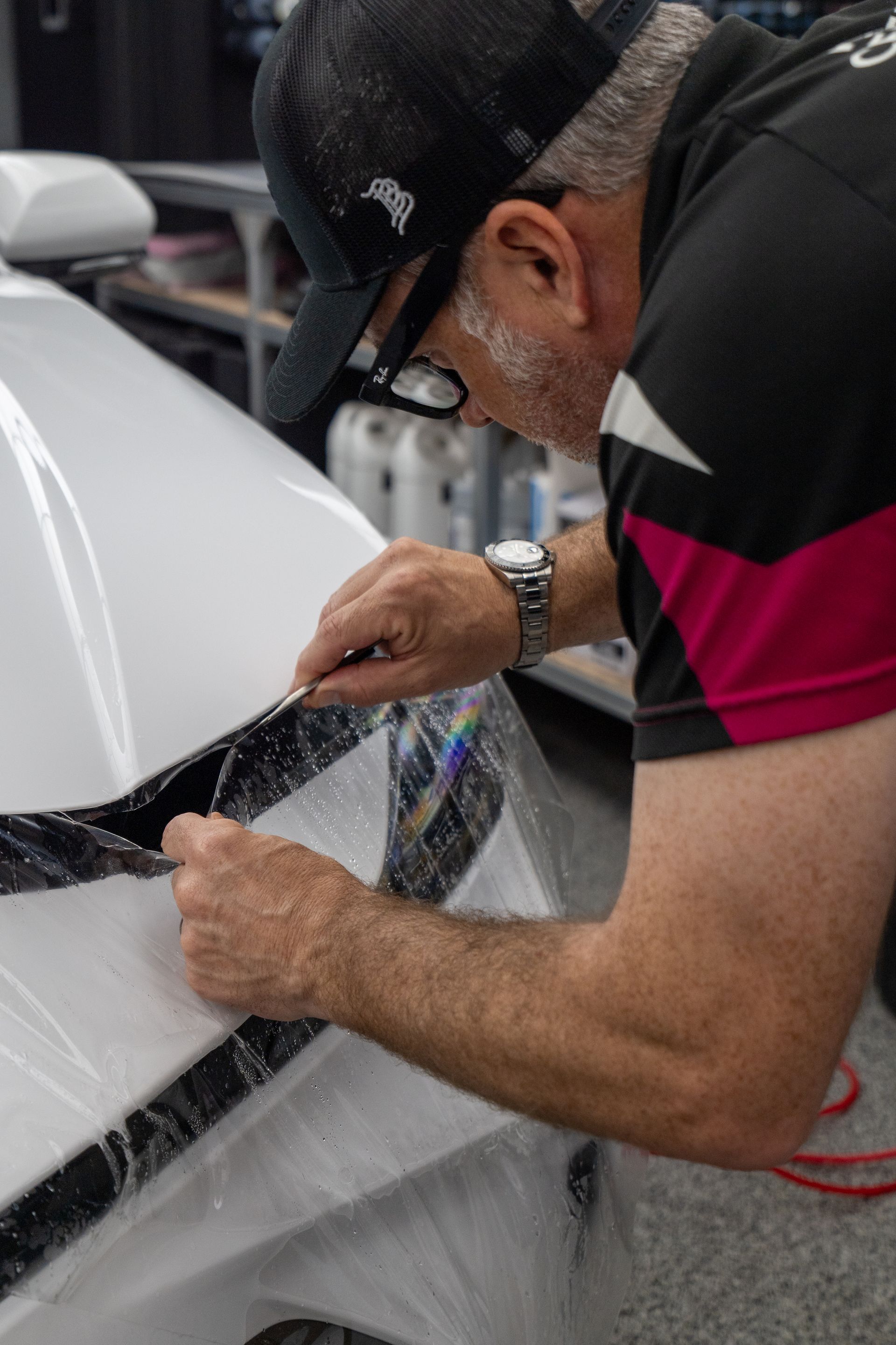 A man is polishing the side mirror of a black car.