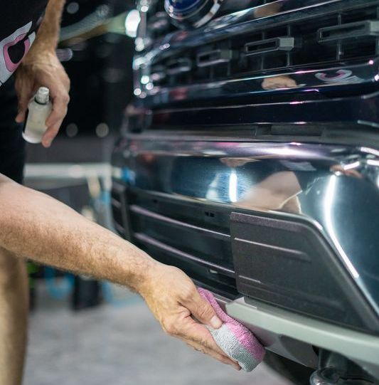 A person is cleaning the front of a truck with a sponge.