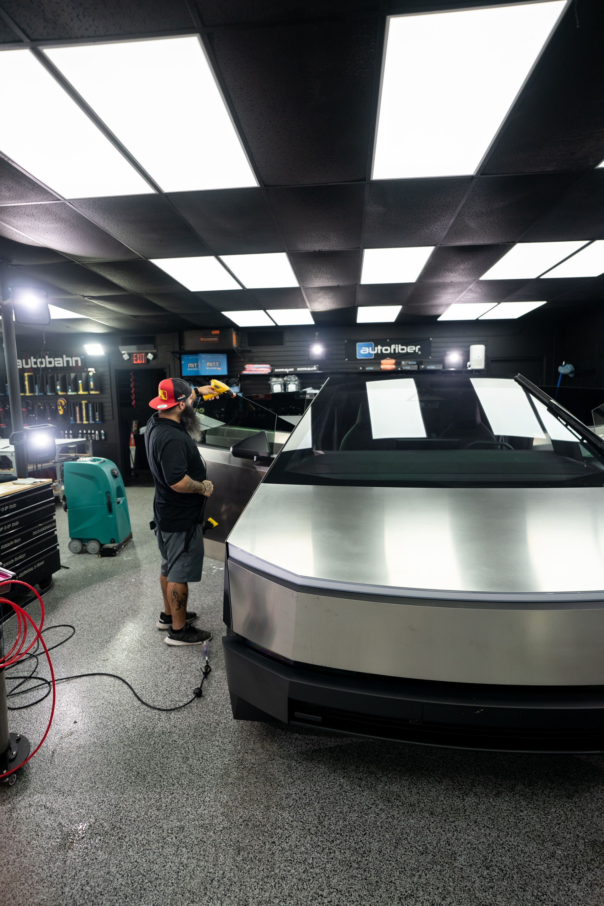 A man is standing next to a silver car in a garage.