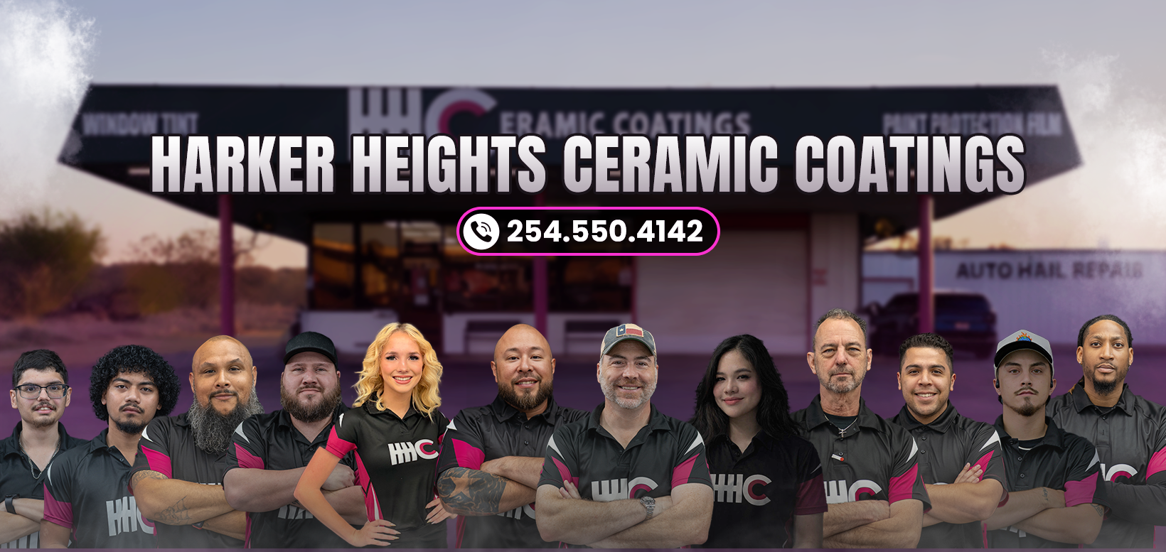 Group of seven people wearing matching black shirts with pink accents, standing in front of a dark wall.