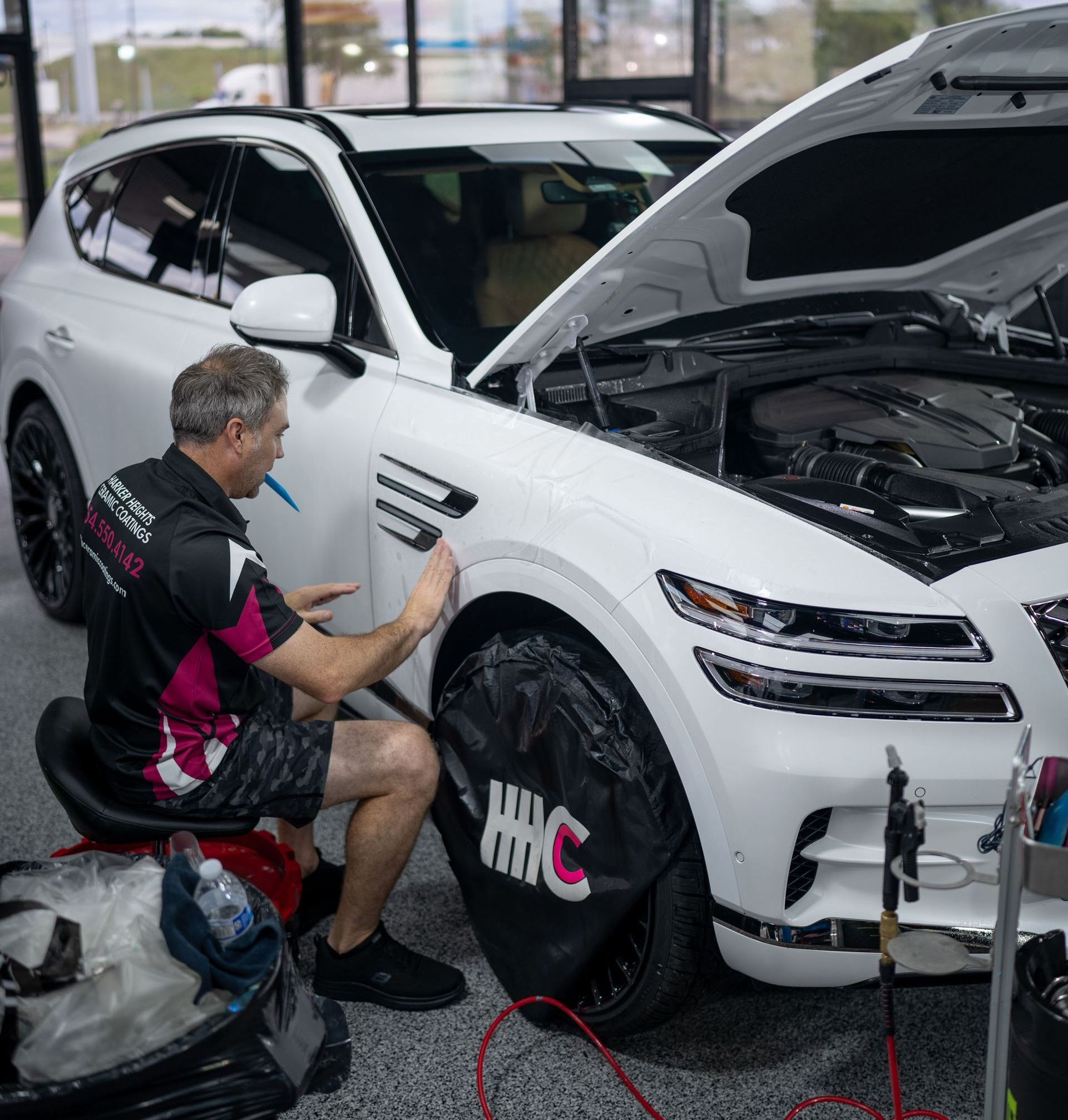 Detailer polishing a white SUV’s front fender in a garage, with hood open and tools nearby