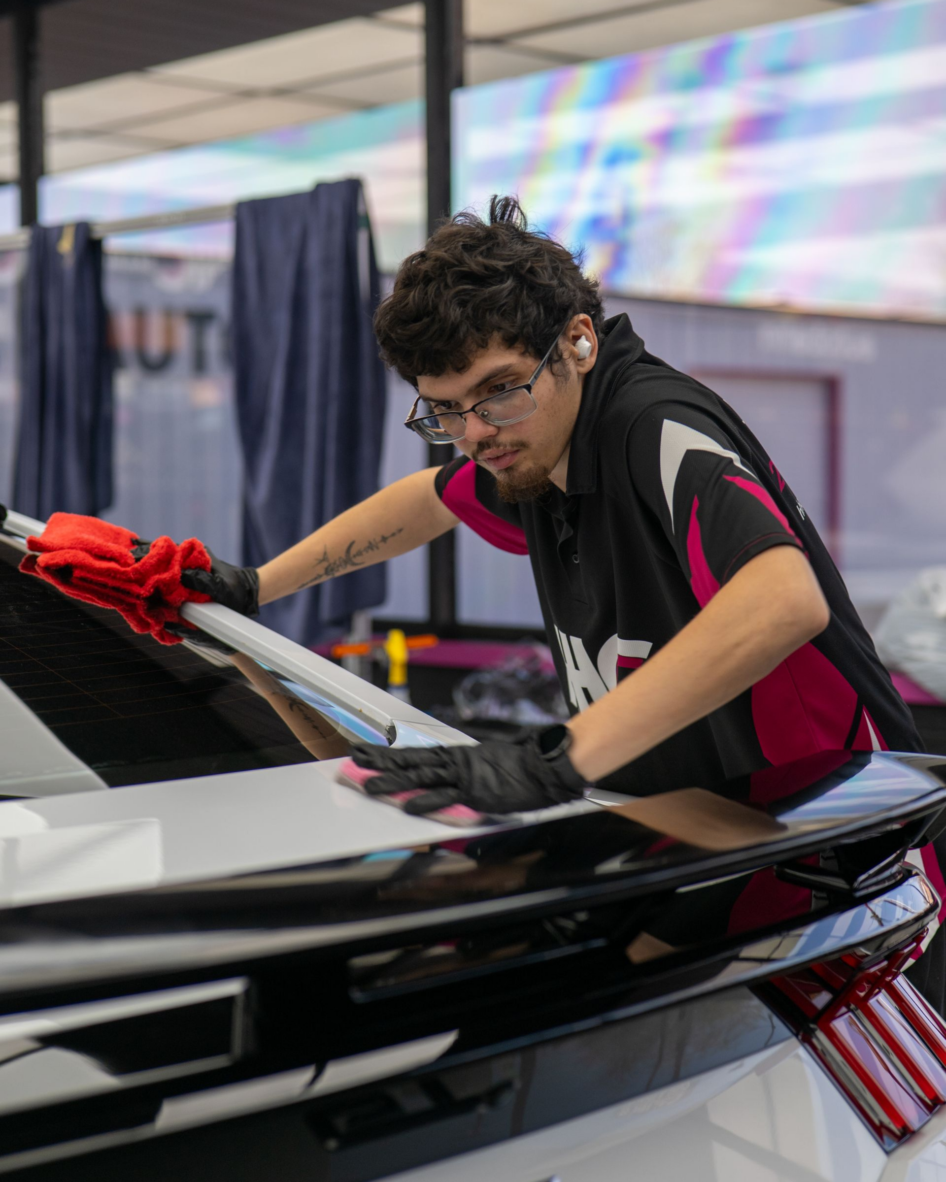 Person polishing a black car with a red cloth at an auto show booth