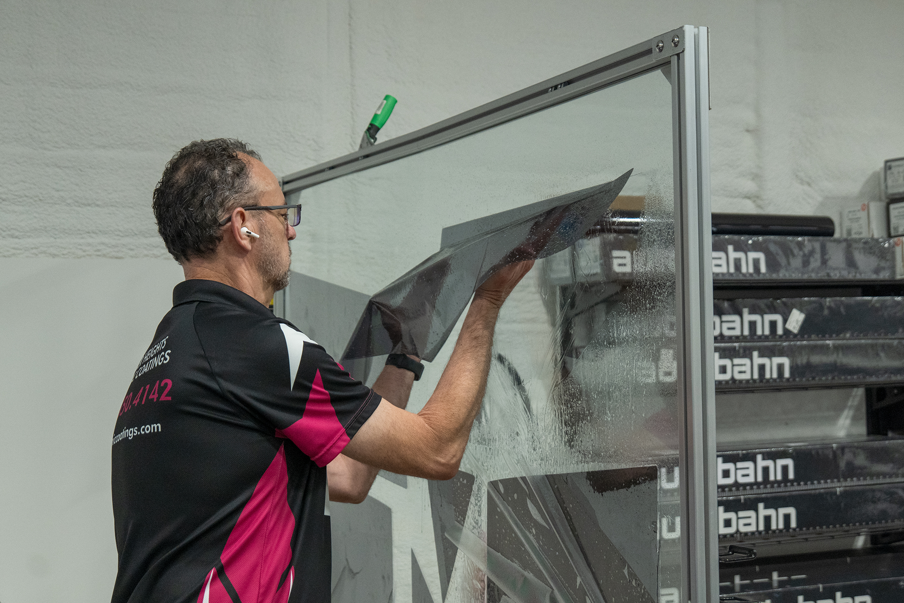 Man installing clear film on a window frame in a workshop